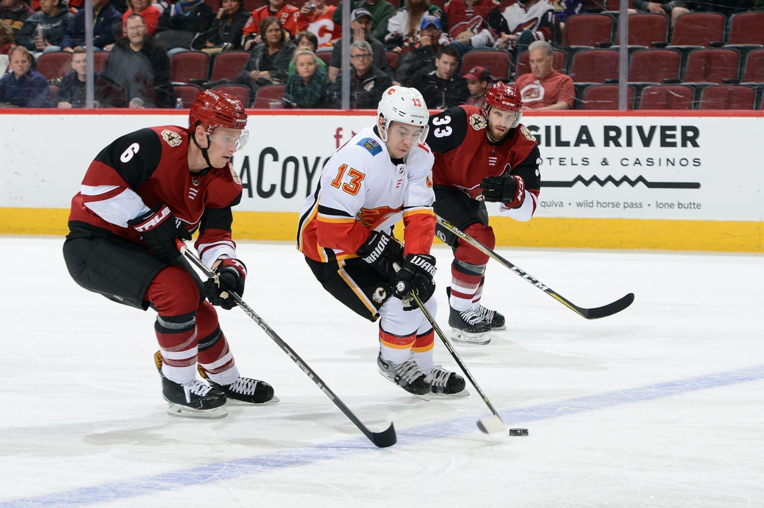GLENDALE, AZ - MARCH 19:  Johnny Gaudreau #13 of the Calgary Flames advances the puck up ice ahead of Jakob Chychrun #6 and Alex Goligoski #33 of the Arizona Coyotes during the first period at Gila River Arena on March 19, 2018 in Glendale, Arizona.  (Photo by Norm Hall/NHLI via Getty Images)