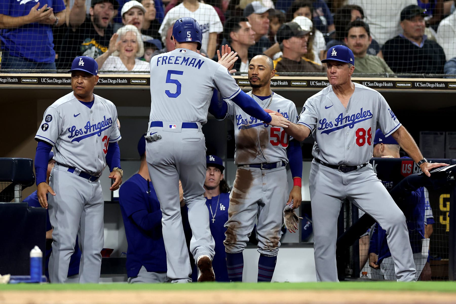 SAN DIEGO, CALIFORNIA - SEPTEMBER 29: Manager Dave Roberts, Mookie Betts #50, and Bob Geren #88 congratulate Freddie Freeman #5 after he scored on an RBI single hit by Miguel Vargas #71 of the Los Angeles Dodgers during the sixth inning of a game against the San Diego Padres at PETCO Park on September 29, 2022 in San Diego, California. (Photo by Sean M. Haffey/Getty Images)