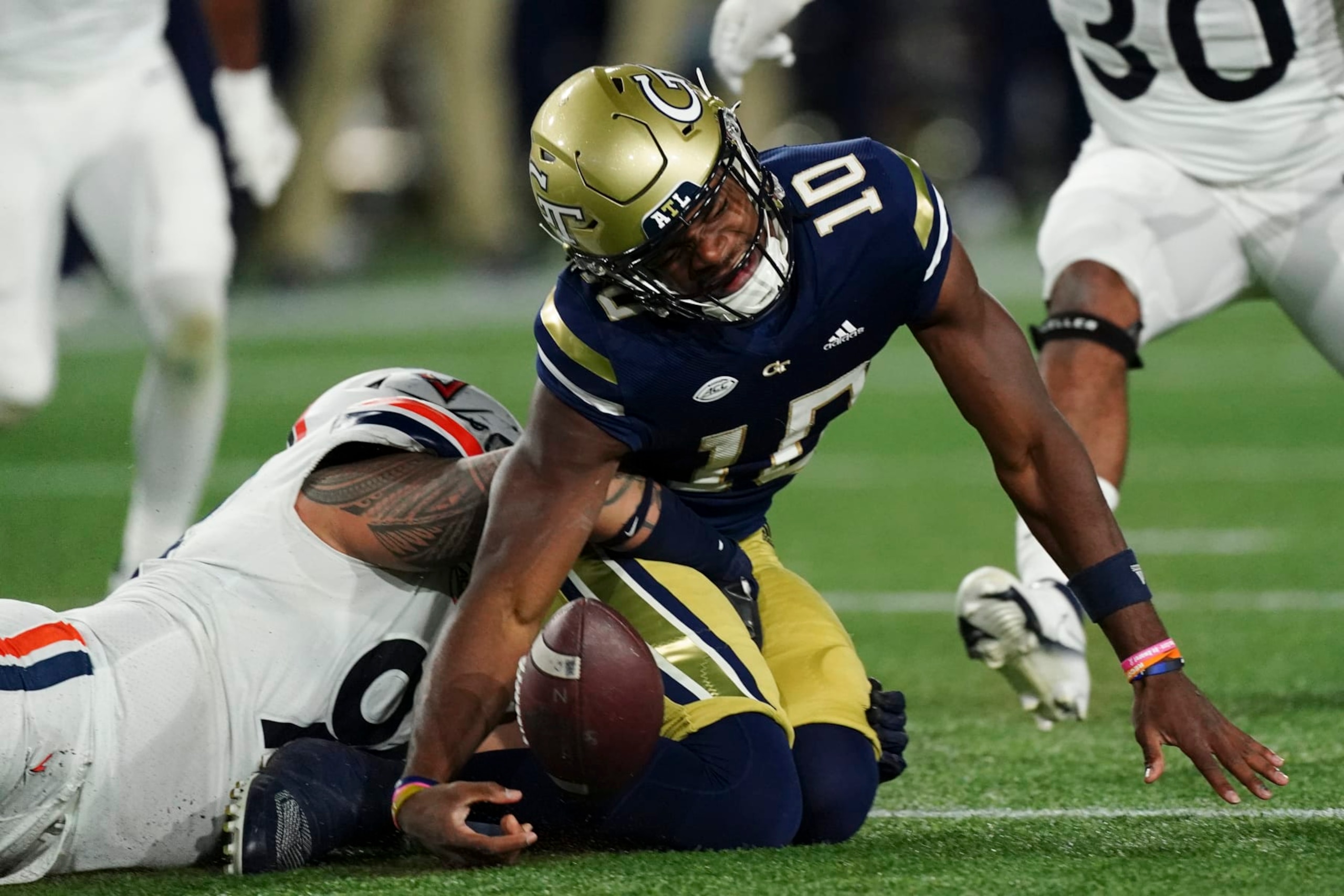 Georgia Tech quarterback Jeff Sims (10) loses the ball as he is tackled by Virginia defensive lineman Aaron Faumui (94) during the first half of an NCAA college football game Thursday, Oct. 20, 2022, in Atlanta. After review, Sims was ruled down before losing the ball. (AP Photo/John Bazemore)