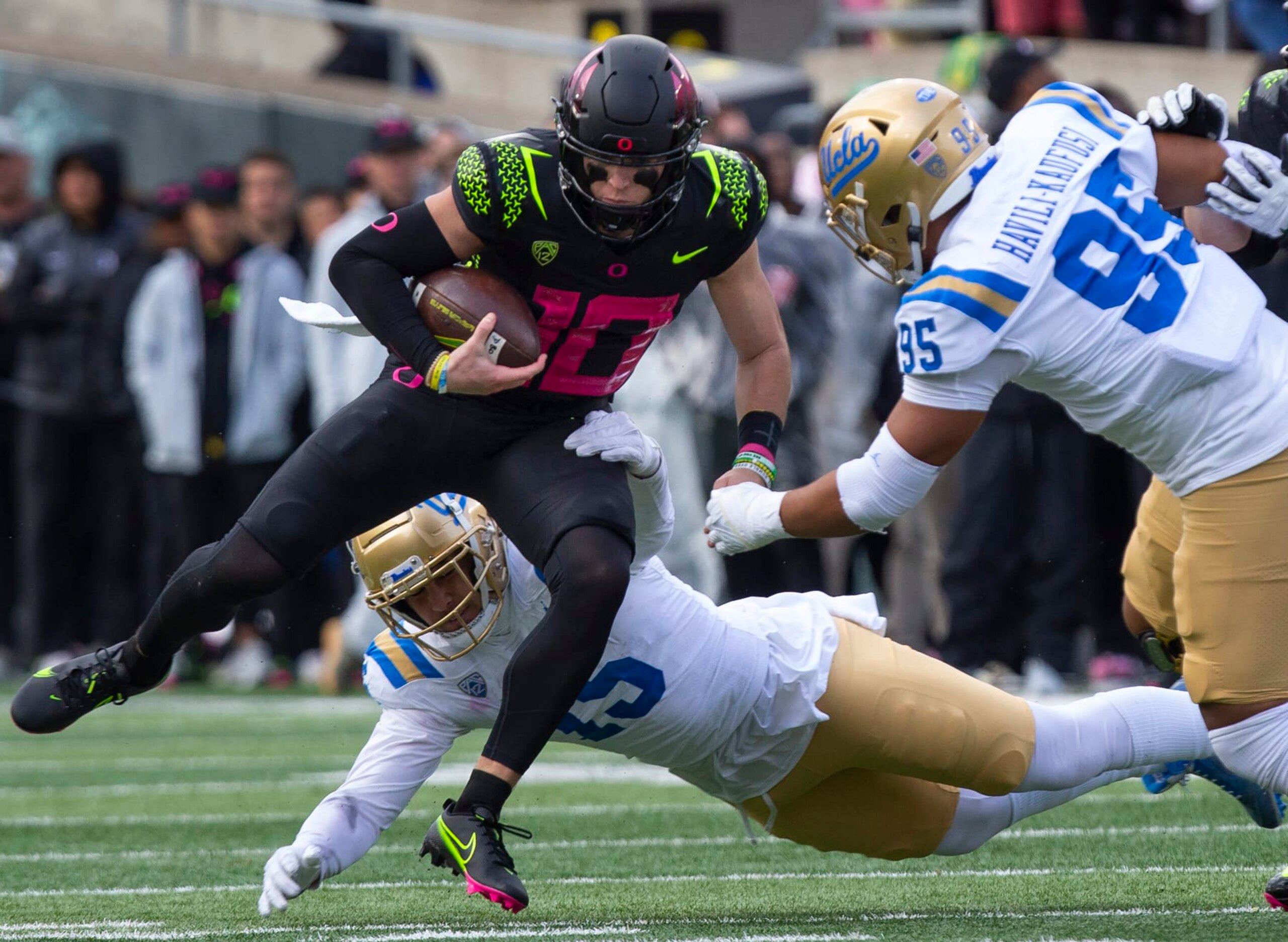 Oregon's Bo Nix, left, rushes against UCLA's Laiatu Latu, bottom and Sitiveni Havili-Kaufusi, right, during the second half in an NCAA college football game Saturday, Oct. 22, 2022, in Eugene, Ore. (AP Photo/Chris Pietsch)