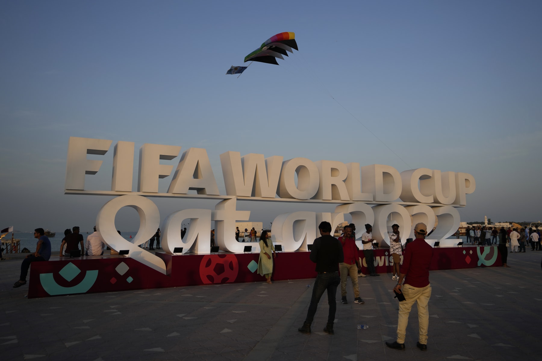 People pose for a photograph with a sign reading in English" Fifa World Cup, Qatar 2022" at the corniche in Doha, Qatar, Friday, Nov. 11, 2022. Final preparations are being made for the soccer World Cup which starts on Nov. 20 when Qatar face Ecuador. (AP Photo/Hassan Ammar)