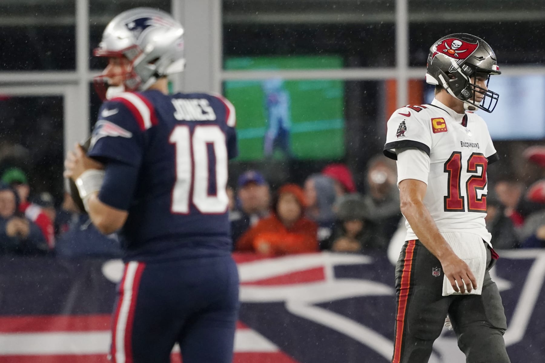 Tampa Bay Buccaneers quarterback Tom Brady (12) walks towards his bench as New England Patriots quarterback Mac Jones (10) warms up prior to an NFL football game between the New England Patriots and Tampa Bay Buccaneers, Sunday, Oct. 3, 2021, in Foxborough, Mass. (AP Photo/Elise Amendola)