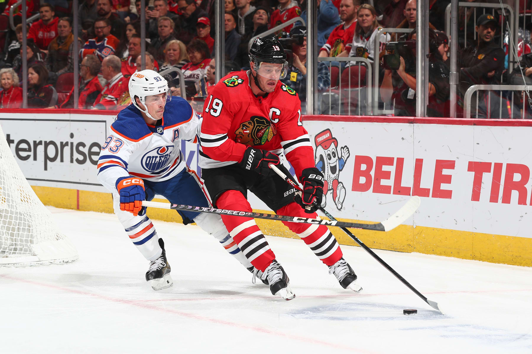 CHICAGO, ILLINOIS - NOVEMBER 30: Jonathan Toews #19 of the Chicago Blackhawks reaches for the puck ahead of Ryan Nugent-Hopkins #93 of the Edmonton Oilers in the first period at United Center on November 30, 2022 in Chicago, Illinois. (Photo by Chase Agnello-Dean/NHLI via Getty Images)