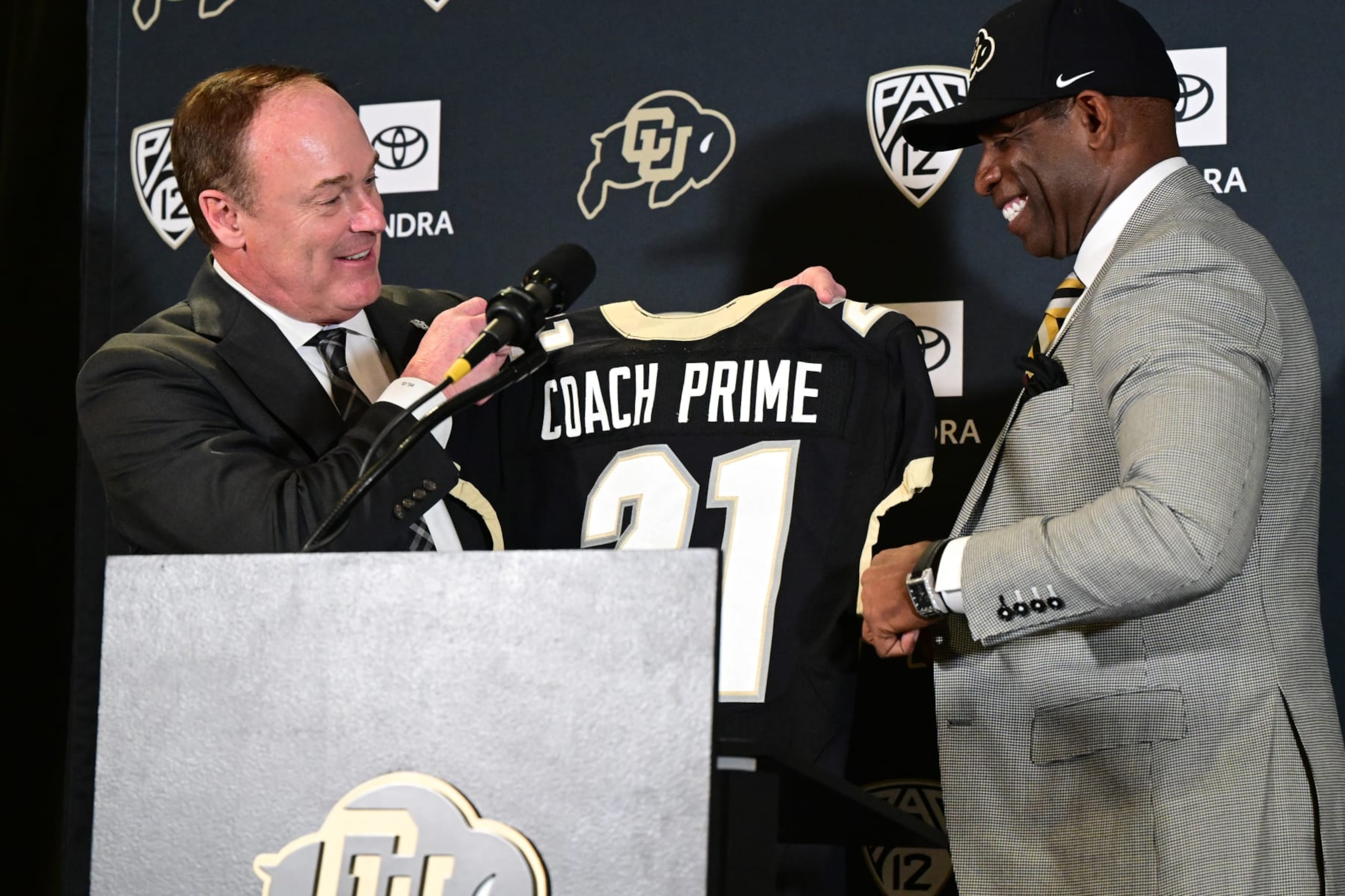 BOULDER, CO - DECEMBER 4:  CU athletic director Rick George, left, gives Deion Sanders, CUs new head football coach a personalized jersey in the Arrow Touchdown Club during a press conference on December 4, 2022 in Boulder, Colorado. CU held an introductory press conference to announce the hiring of Deion Coach Prime Sanders as the schools new head football coach. Chancellor Phil DiStefano and athletic director Rick George accompanied Sanders into a packed room in the Arrow Touchdown Club inside the Dal Ward Athletic Center. Sanders becomes the 28th head coach in Buffalo football history.  Sanders, who known as Prime Time during his Hall of Fame playing career has since transitioned into Coach Prime as a head football coach. Sanders, 55, joins the CU program from Jackson State University where in three seasons the Tigers compiled a 27-5 record and won back-to-back Southwestern Athletic Conference championships. (Photo by Helen H. Richardson/MediaNews Group/The Denver Post via Getty Images)