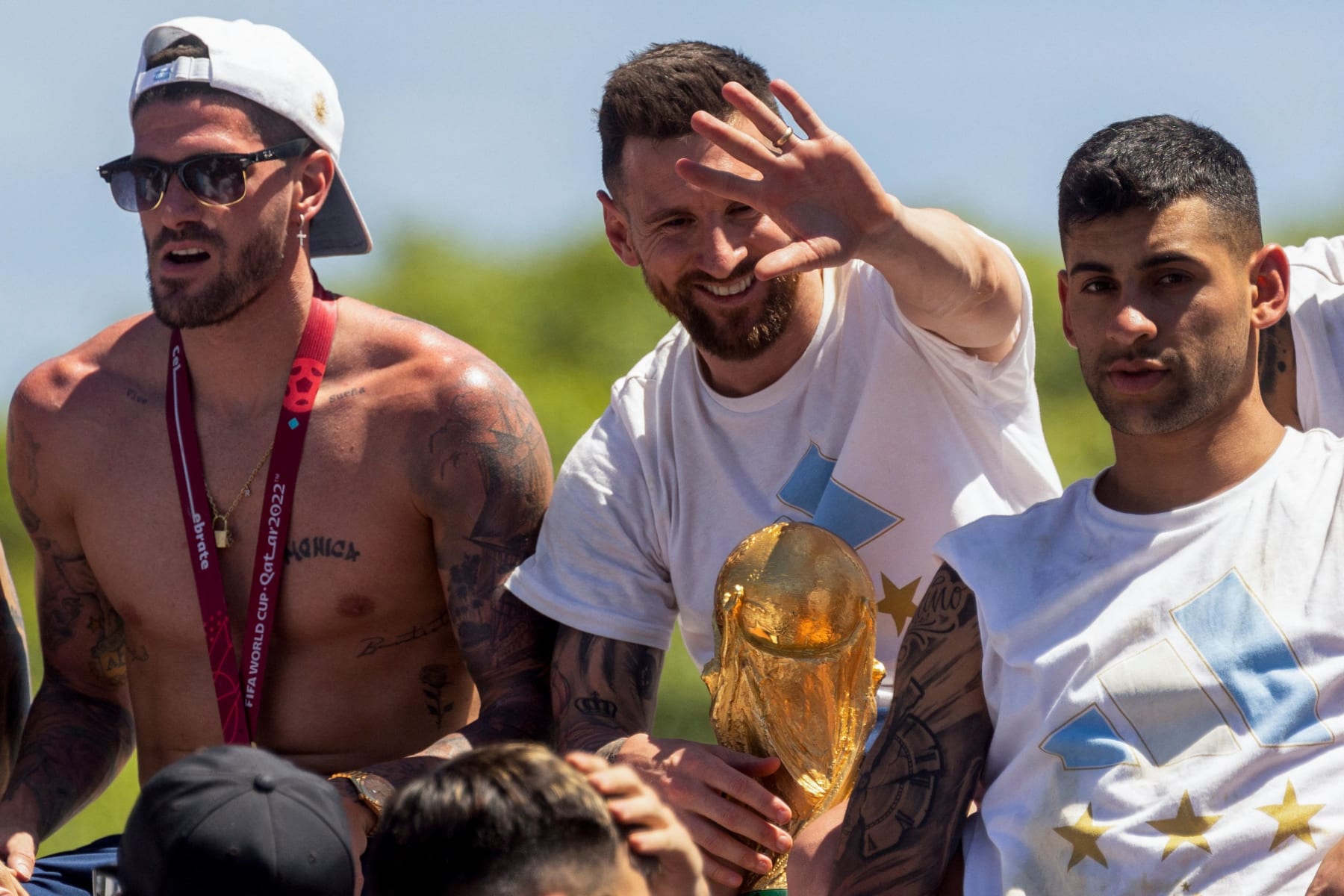 Argentine players Rodrigo De Paul (L), Lionel Messi (C) and Cristian Romero (R) celebrate on board a bus with a sign reading "World Champions" with supporters after winning the Qatar 2022 World Cup tournament as they tour through Buenos Aires' downtown on December 20, 2022. - Millions of ecstatic fans are expected to cheer on their heroes as Argentina's World Cup winners led by captain Lionel Messi began their open-top bus parade of the capital Buenos Aires on Tuesday following their sensational victory over France. (Photo by TOMAS CUESTA / AFP) (Photo by TOMAS CUESTA/AFP via Getty Images)