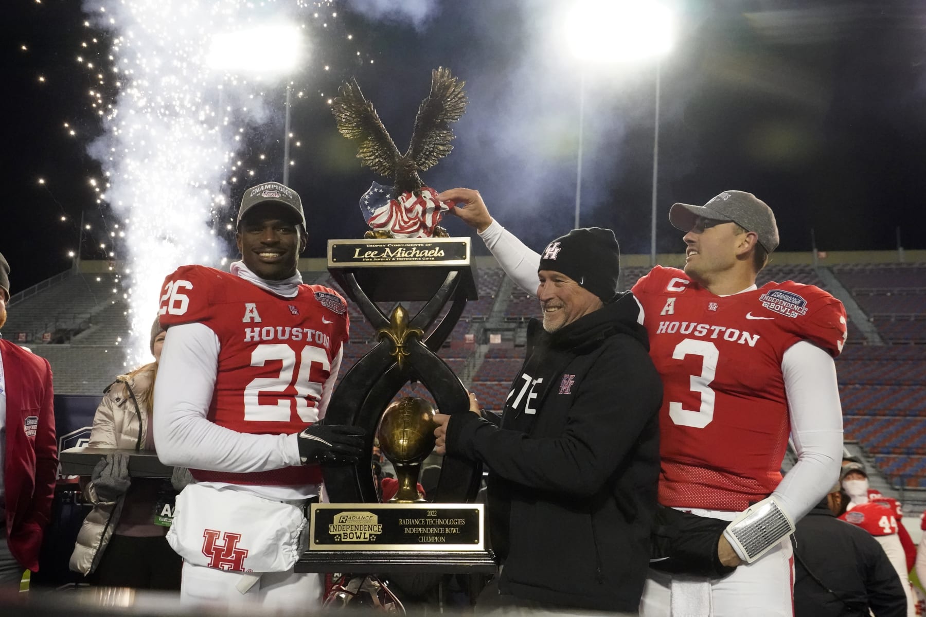 CORRECTS TO ART GREEN NOT MOSES ALEXANDER - Houston head coach Dana Holgorsen, center, looks on as he and defensive back Art Green (26) and quarterback Clayton Tune (3) hoist the Independence Bowl championship trophy following their win over Louisiana-Lafayette in an NCAA college football game Friday, Dec. 23, 2022, in Shreveport, La. (AP Photo/Rogelio V. Solis)