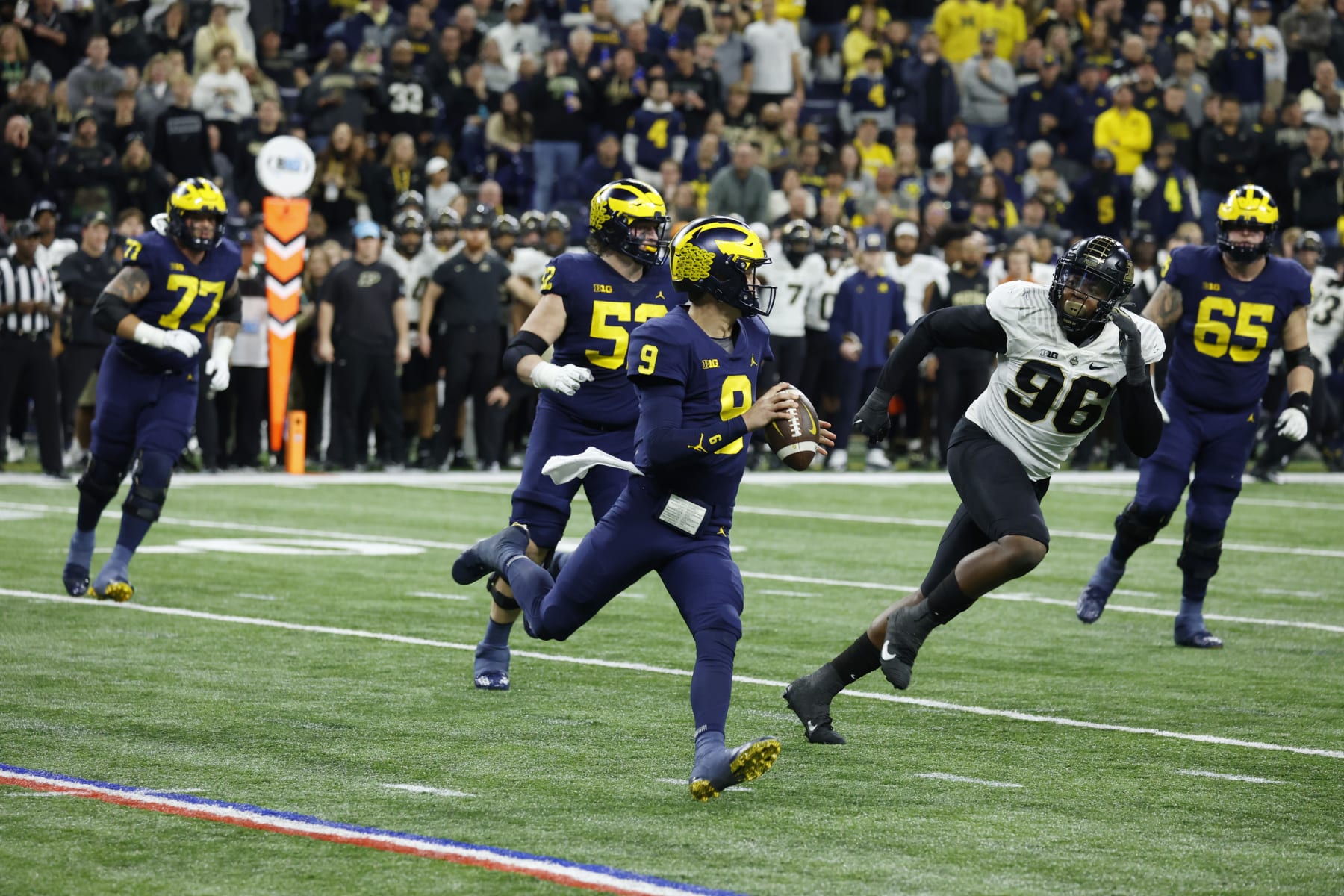 INDIANAPOLIS, IN - DECEMBER 03: Michigan Wolverines quarterback J.J. McCarthy (9) rolls out to throw a pass while chased by Purdue Boilermakers defensive end Khordae Sydney (96) on December 3, 2022, during the Big 10 Football Championship at Lucas Oil Stadium in Indianapolis, Indiana. (Photo by Brian Spurlock/Icon Sportswire via Getty Images)