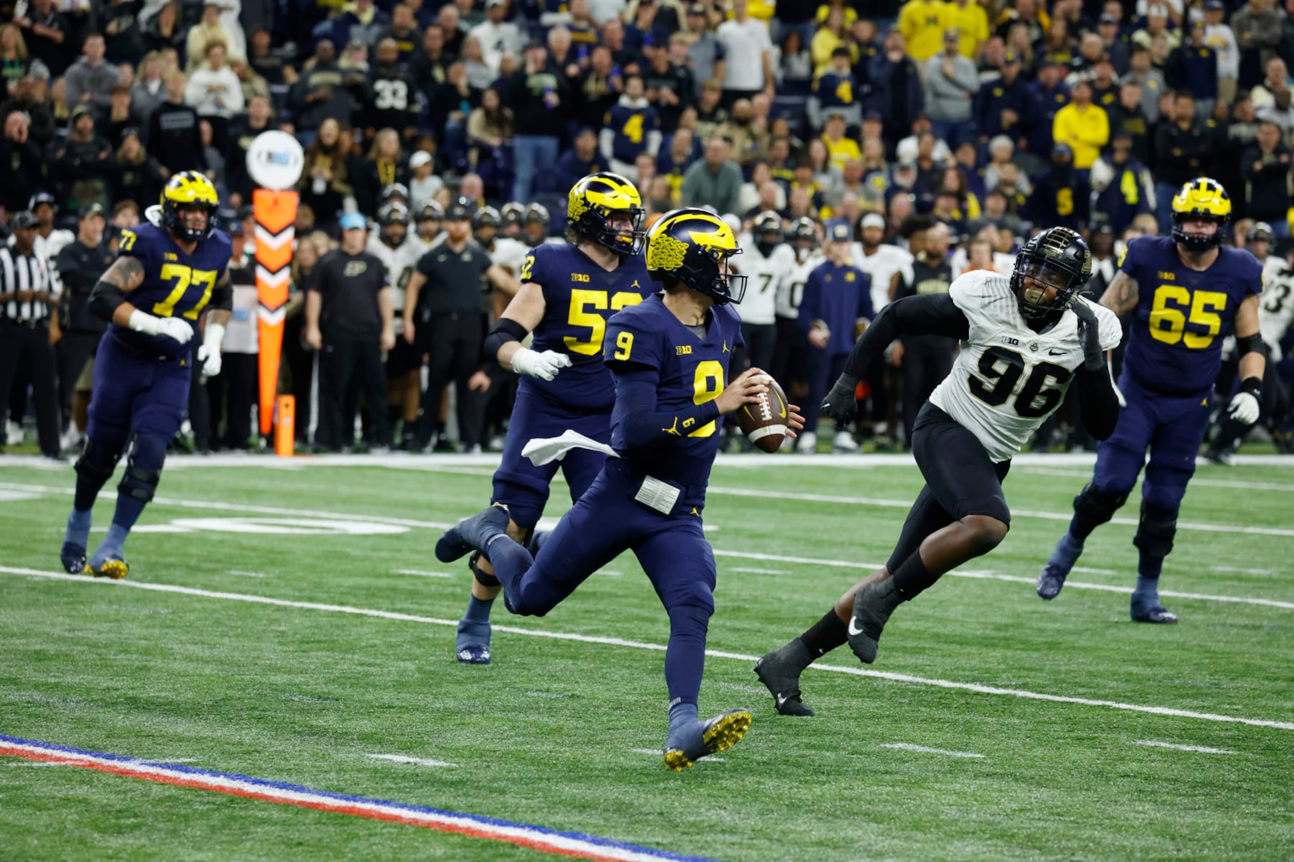 INDIANAPOLIS, IN - DECEMBER 03: Michigan Wolverines quarterback J.J. McCarthy (9) rolls out to throw a pass while chased by Purdue Boilermakers defensive end Khordae Sydney (96) on December 3, 2022, during the Big 10 Football Championship at Lucas Oil Stadium in Indianapolis, Indiana. (Photo by Brian Spurlock/Icon Sportswire via Getty Images)