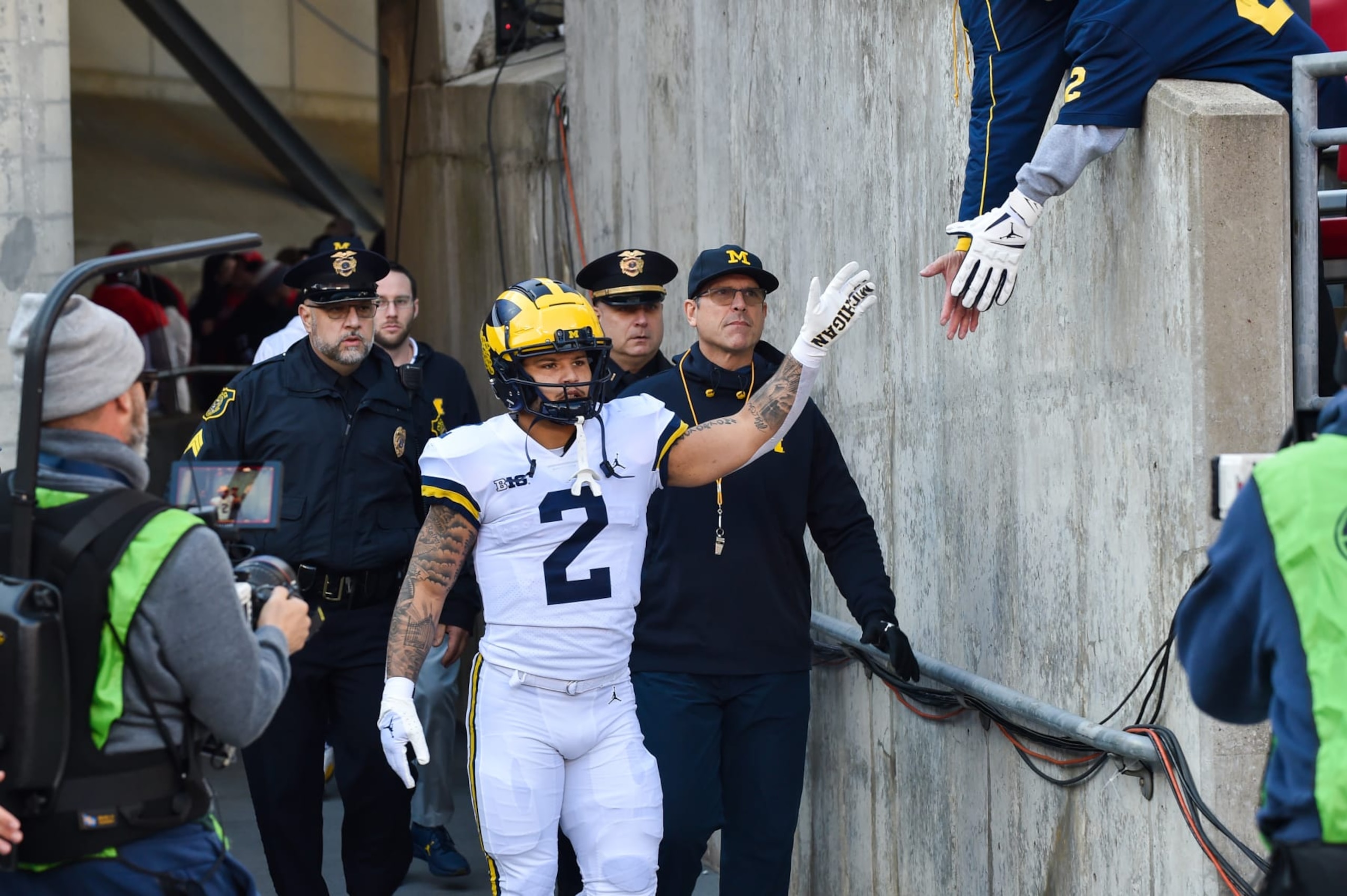 COLUMBUS, OHIO - NOVEMBER 26: Head Football Coach Jim Harbaugh (R) and Blake Corum #2 (C) of the Michigan Wolverines slap hands with fans as they walk out of the tunnel before a college football game against the Ohio State Buckeyes at Ohio Stadium on November 26, 2022 in Columbus, Ohio. (Photo by Aaron J. Thornton/Getty Images)