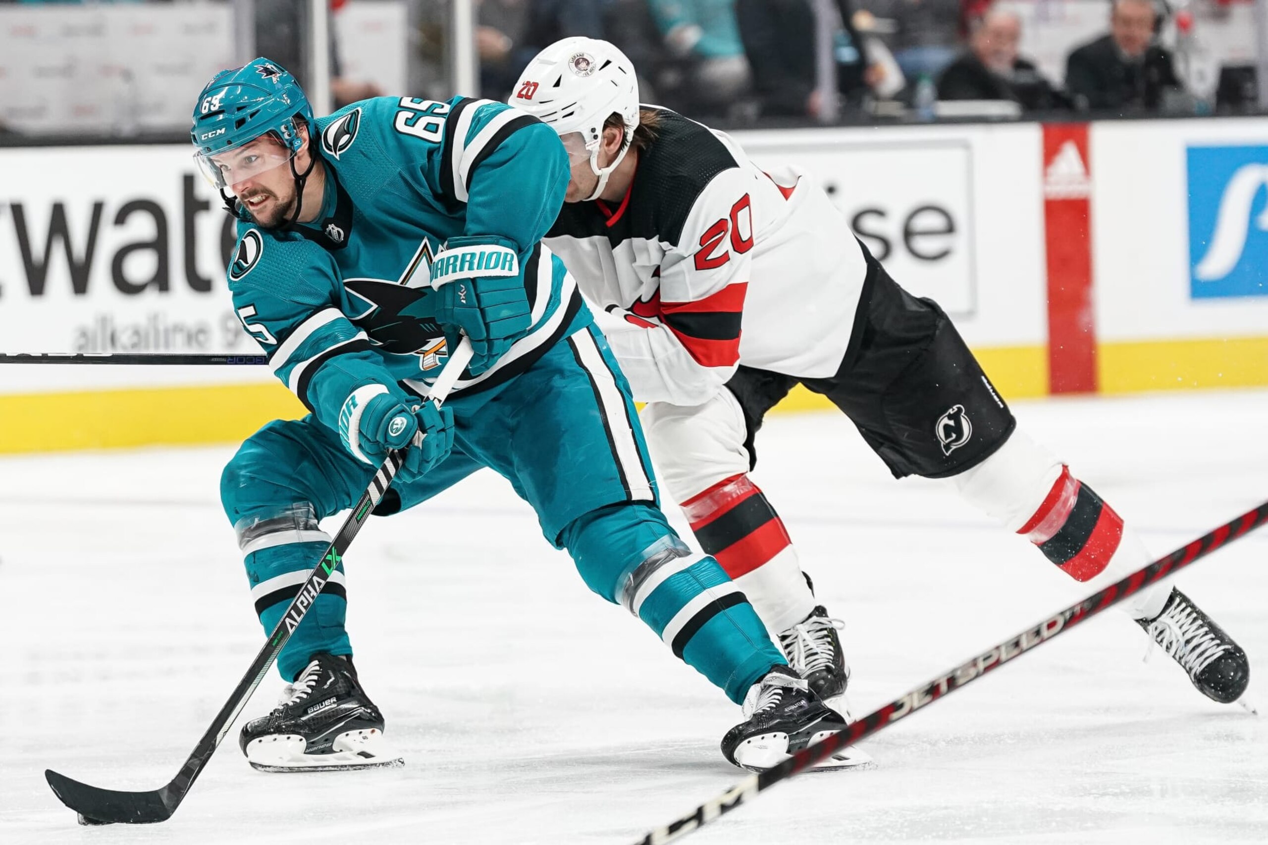 SAN JOSE, CA - JANUARY 16: Erik Karlsson #65 of the San Jose Sharks skates with the puck against Michael McLeod #20 of the New Jersey Devils at SAP Center on January 16, 2023 in San Jose, California. (Photo by Kavin Mistry/NHLI via Getty Images)