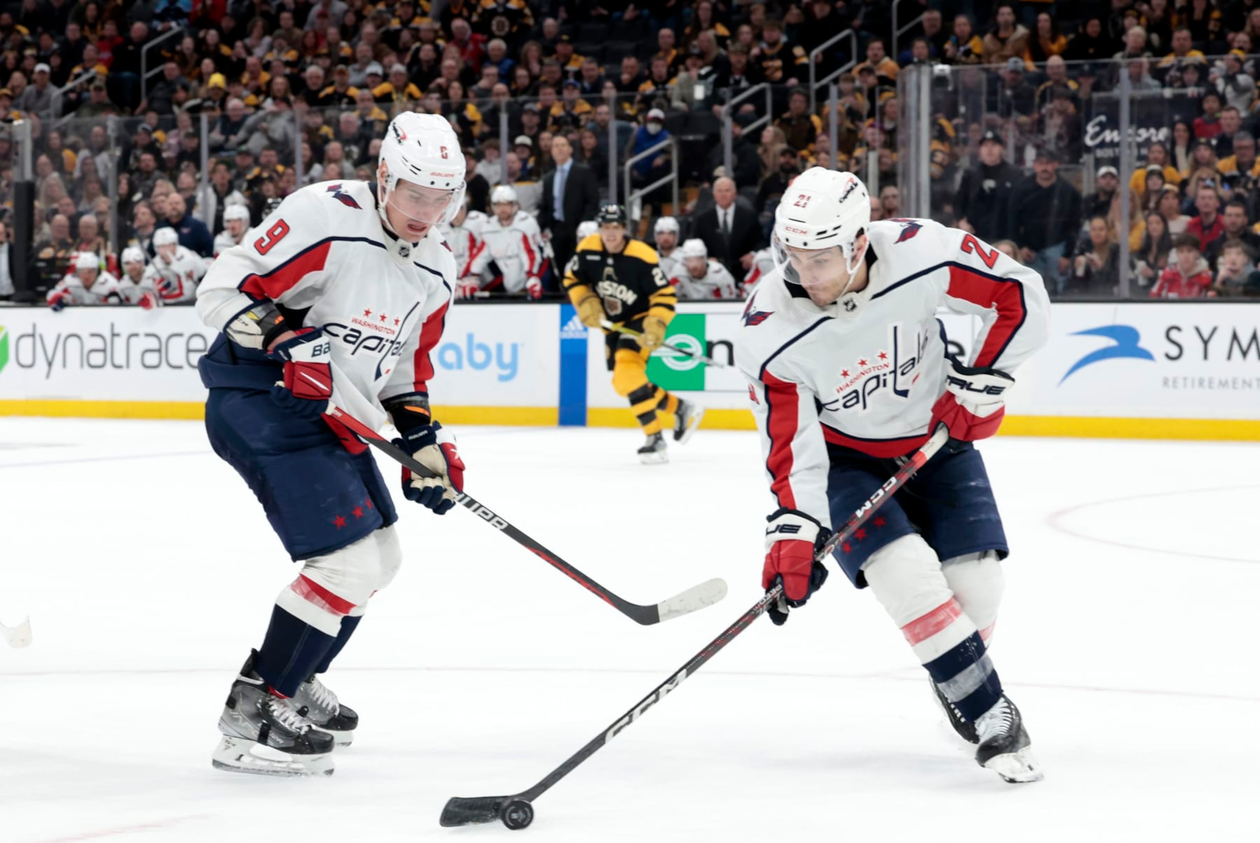BOSTON, MA - FEBRUARY 11: Washington Capitals right wing Garnet Hathaway (21) grabs the puck watched by defenseman Dmitry Orlov (9) during a game between the Boston Bruins and the Washington Capitals on February 11, 2023, at TD Garden in Boston, Massachusetts. (Photo by Fred Kfoury III/Icon Sportswire via Getty Images)
