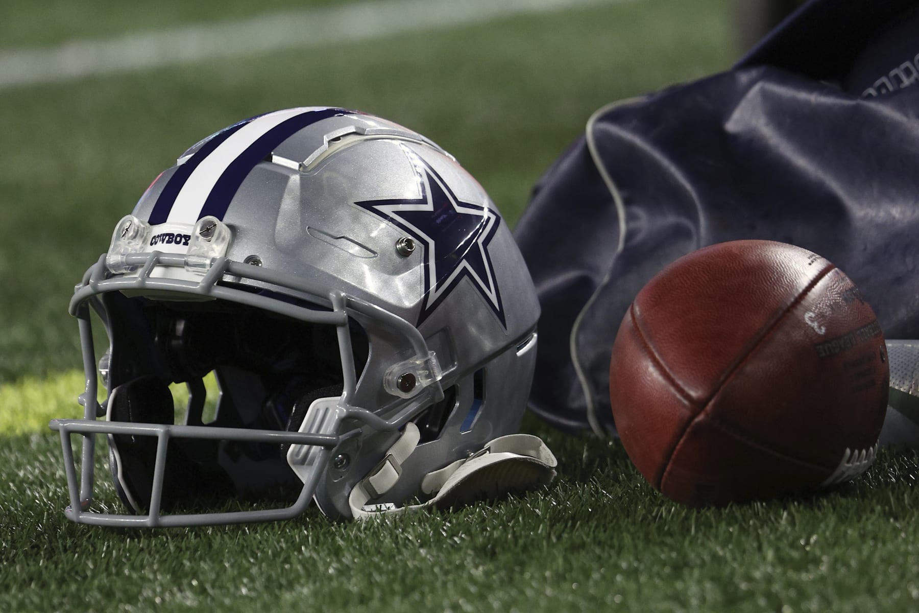 A helmet with the Dallas Cowboys logo is seen next to a football during an NFL football game between the New England Patriots and the Dallas Cowboys at Gillette Stadium, Sunday, Oct. 17, 2021 in Foxborough, Mass. (Winslow Townson/AP Images for Panini)