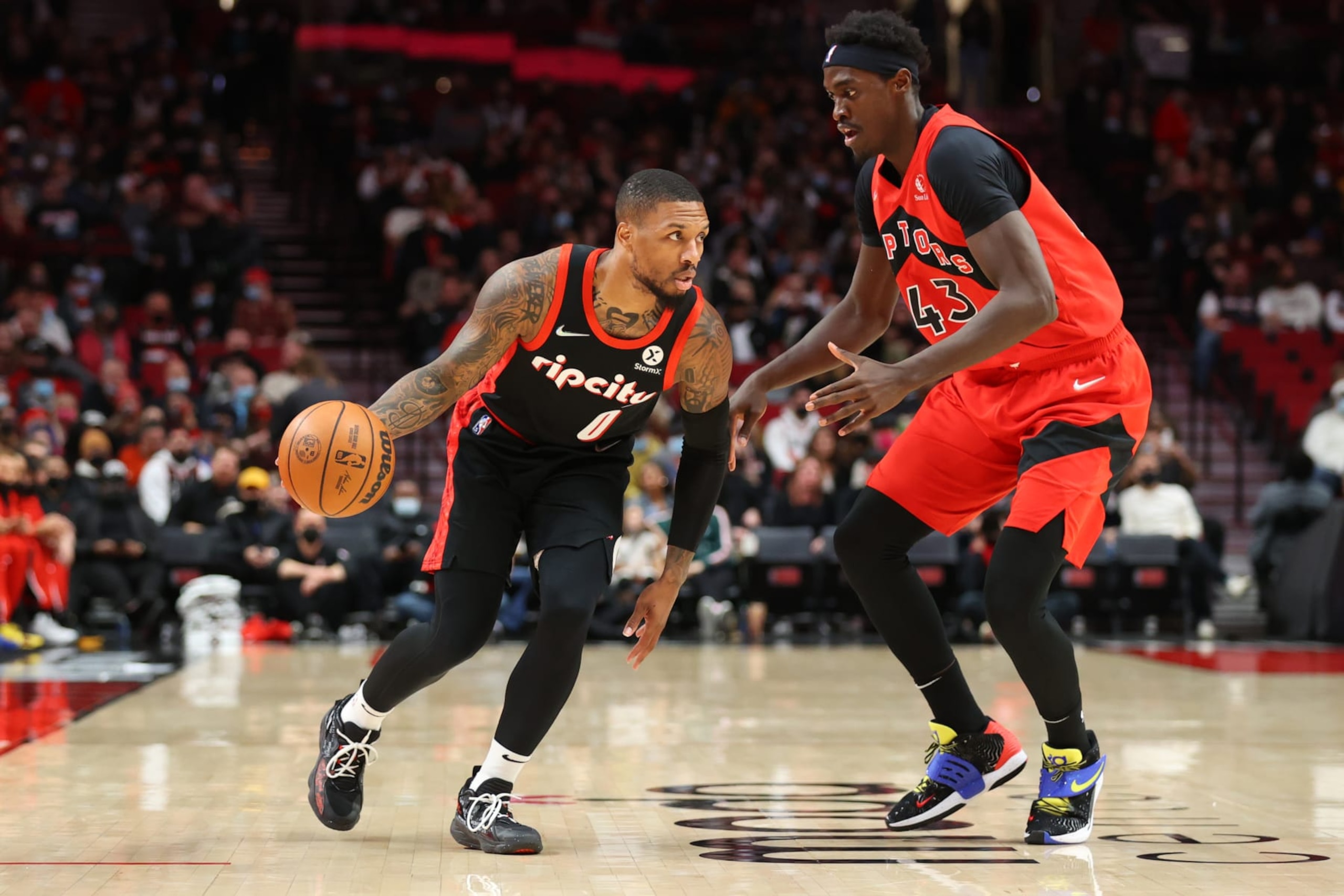 PORTLAND, OREGON - NOVEMBER 15: Damian Lillard #0 of the Portland Trail Blazers dribbles against Pascal Siakam #43 of the Toronto Raptors during the first quarter at Moda Center on November 15, 2021 in Portland, Oregon.  NOTE TO USER: User expressly acknowledges and agrees that, by downloading and or using this photograph, User is consenting to the terms and conditions of the Getty Images License Agreement. (Photo by Abbie Parr/Getty Images)