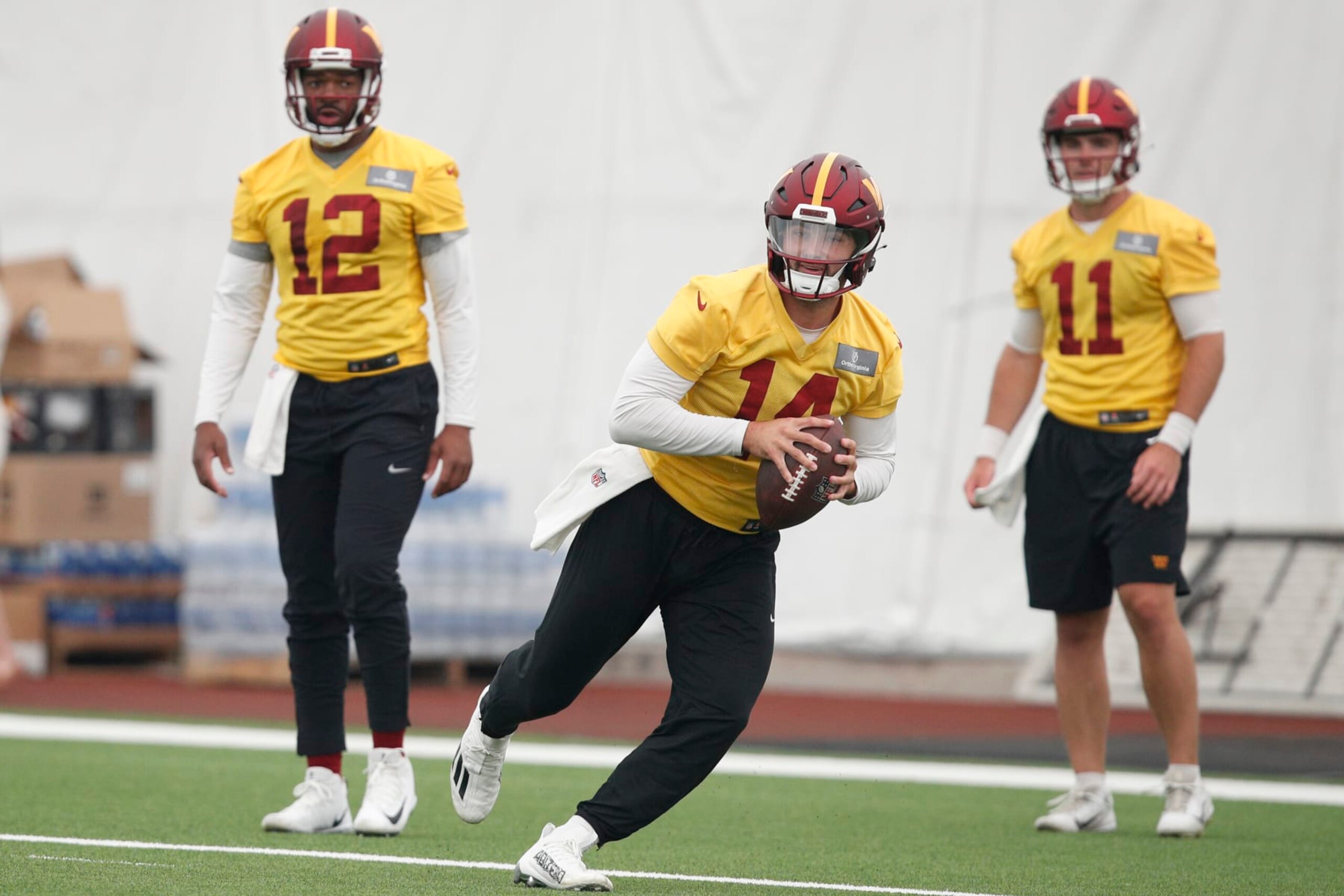 Washington Commanders quarterback Sam Howell (14) scrambles as quarterbacks Jacoby Brissett (12) and Jake Fromm (11) look on during an NFL football practice at the team's indoor training facility in Ashburn, Va., Thursday, June 8, 2023. (AP Photo/Luis M. Alvarez)