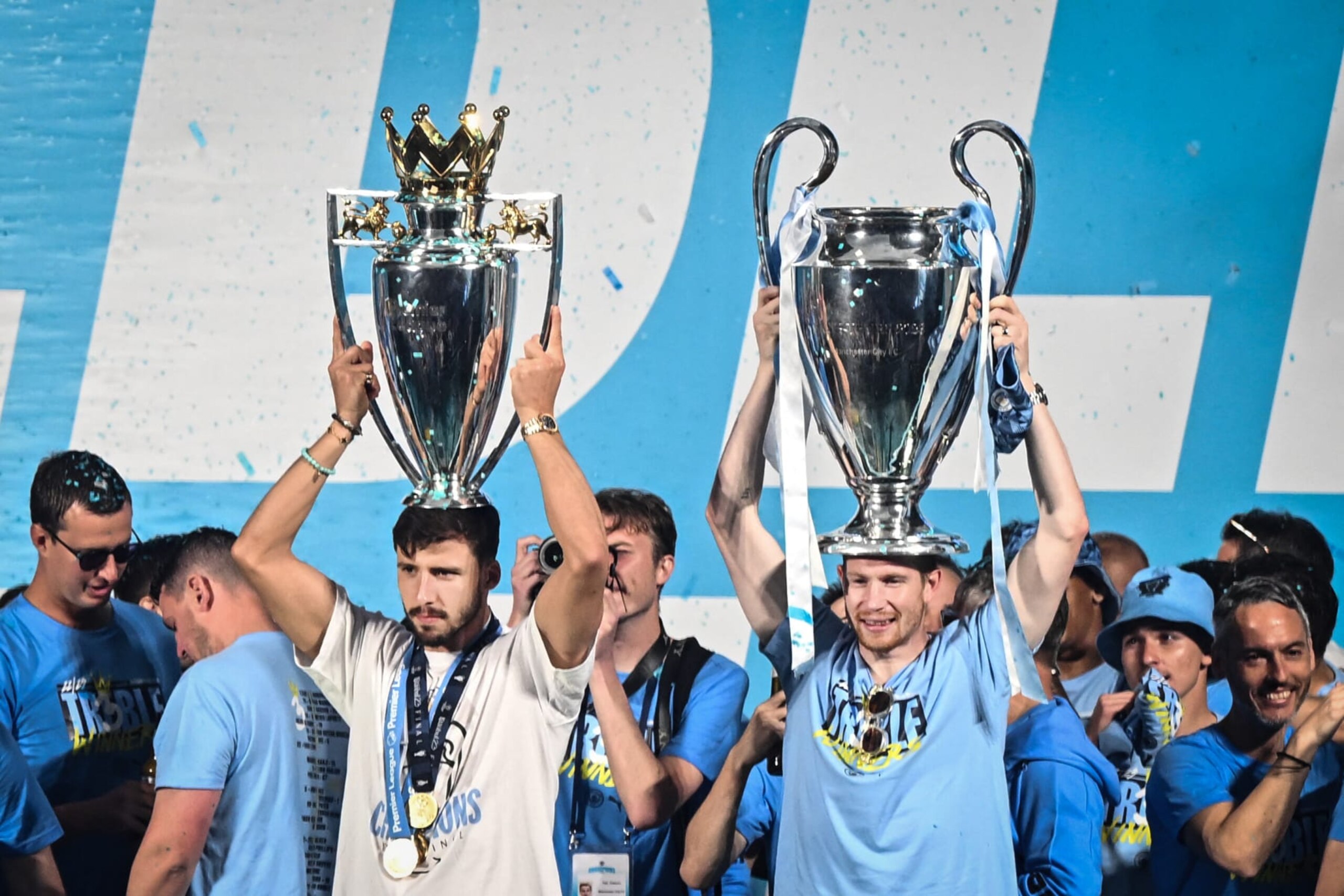 Manchester City's Portuguese defender Ruben Dias (L) and Manchester City's Belgian midfielder Kevin De Bruyne (R) celebrate with their trophies on stage following an open-top bus victory parade for their European Cup, FA Cup and Premier League victories, in Manchester, northern England on June 12, 2023. Manchester City tasted Champions League glory at last on Saturday as a second-half Rodri strike gave the favourites a 1-0 victory over Inter Milan in a tense final, allowing Pep Guardiola's side to complete a remarkable treble. Having already claimed a fifth Premier League title in six seasons, and added the FA Cup, City are the first English club to win such a treble since Manchester United in 1999. (Photo by Oli SCARFF / AFP) (Photo by OLI SCARFF/AFP via Getty Images)