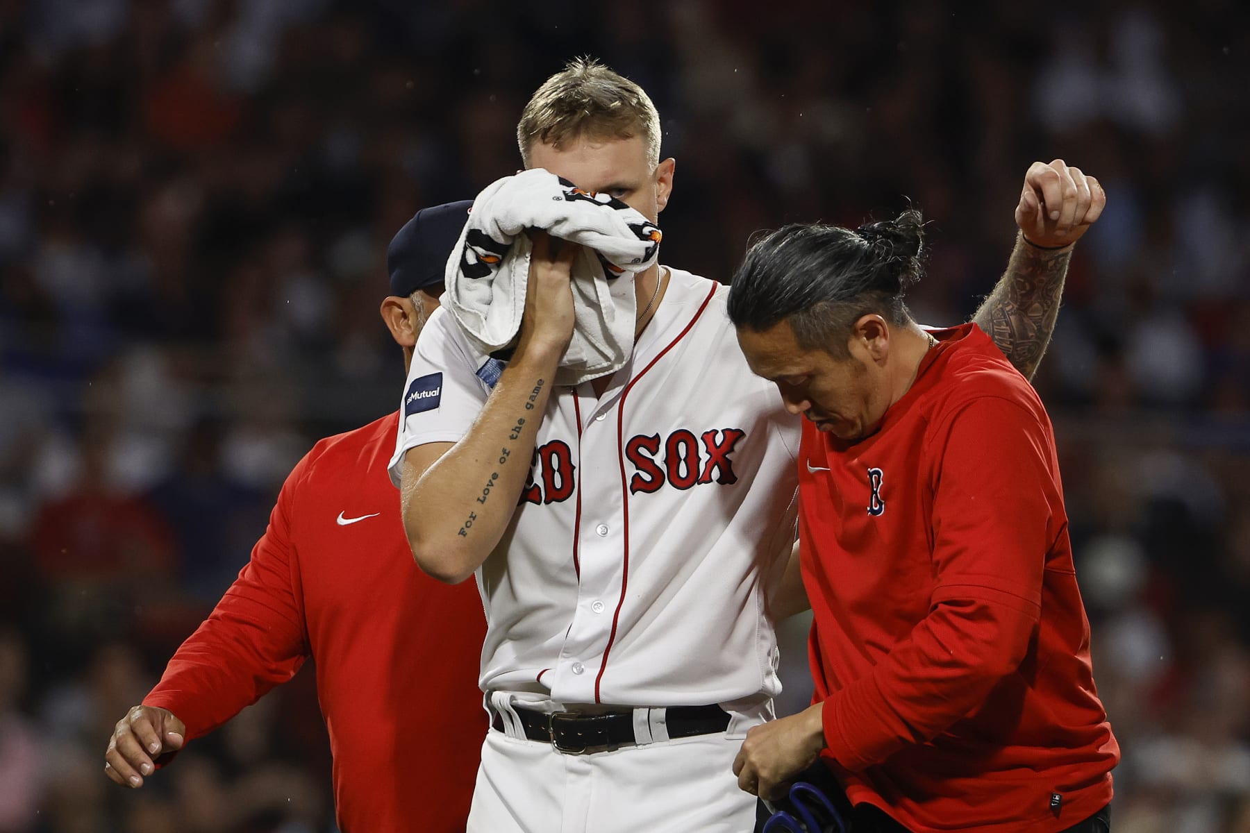 Boston Red Sox starting pitcher Tanner Houck holds a towel to his face as is helped off the field by a trainer after being struck by a line drive on the cheek during the fifth inning of a baseball game against the New York Yankees, Friday, June 16, 2023, at Fenway Park in Boston. (AP Photo/Winslow Townson)