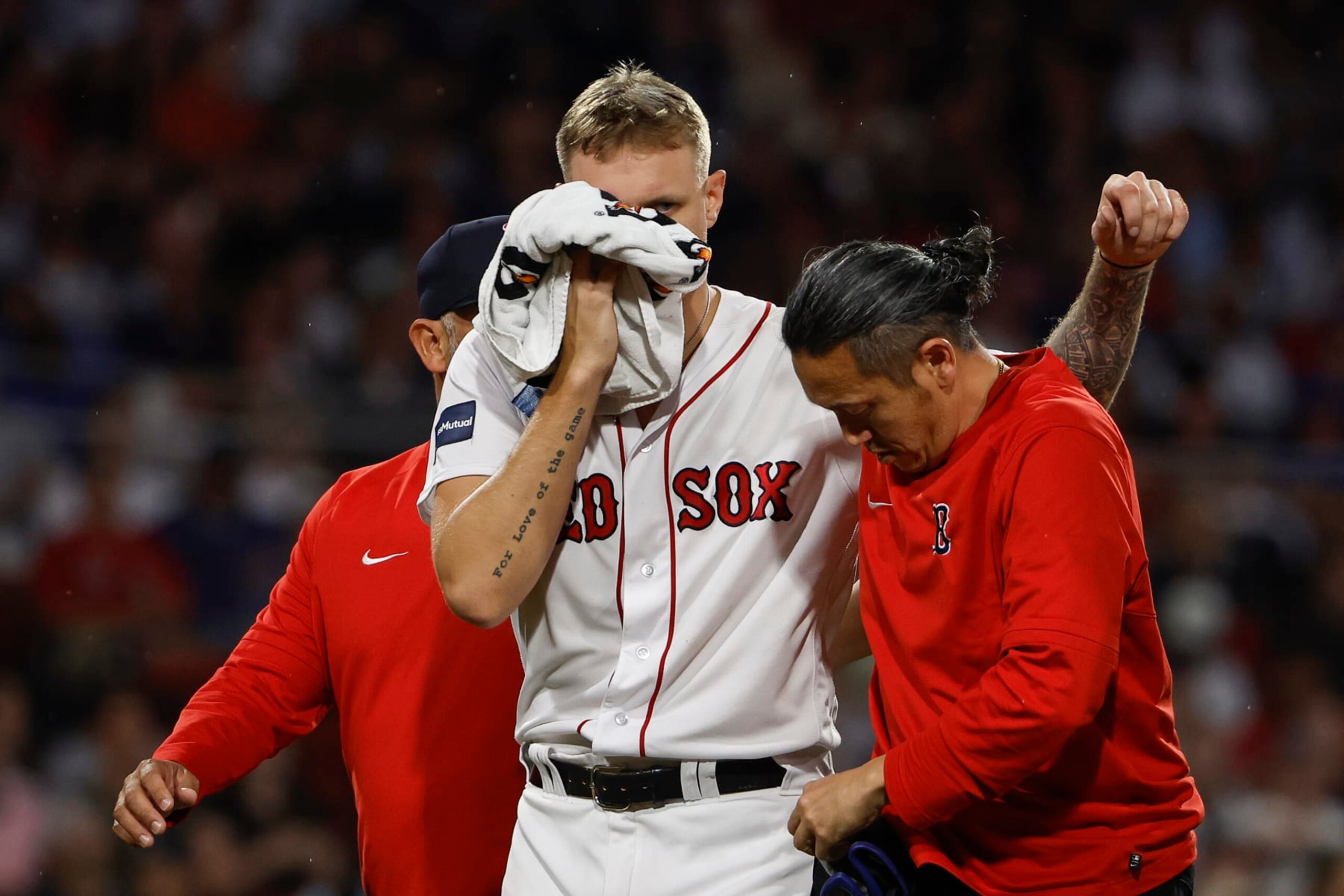 Boston Red Sox starting pitcher Tanner Houck holds a towel to his face as is helped off the field by a trainer after being struck by a line drive on the cheek during the fifth inning of a baseball game against the New York Yankees, Friday, June 16, 2023, at Fenway Park in Boston. (AP Photo/Winslow Townson)