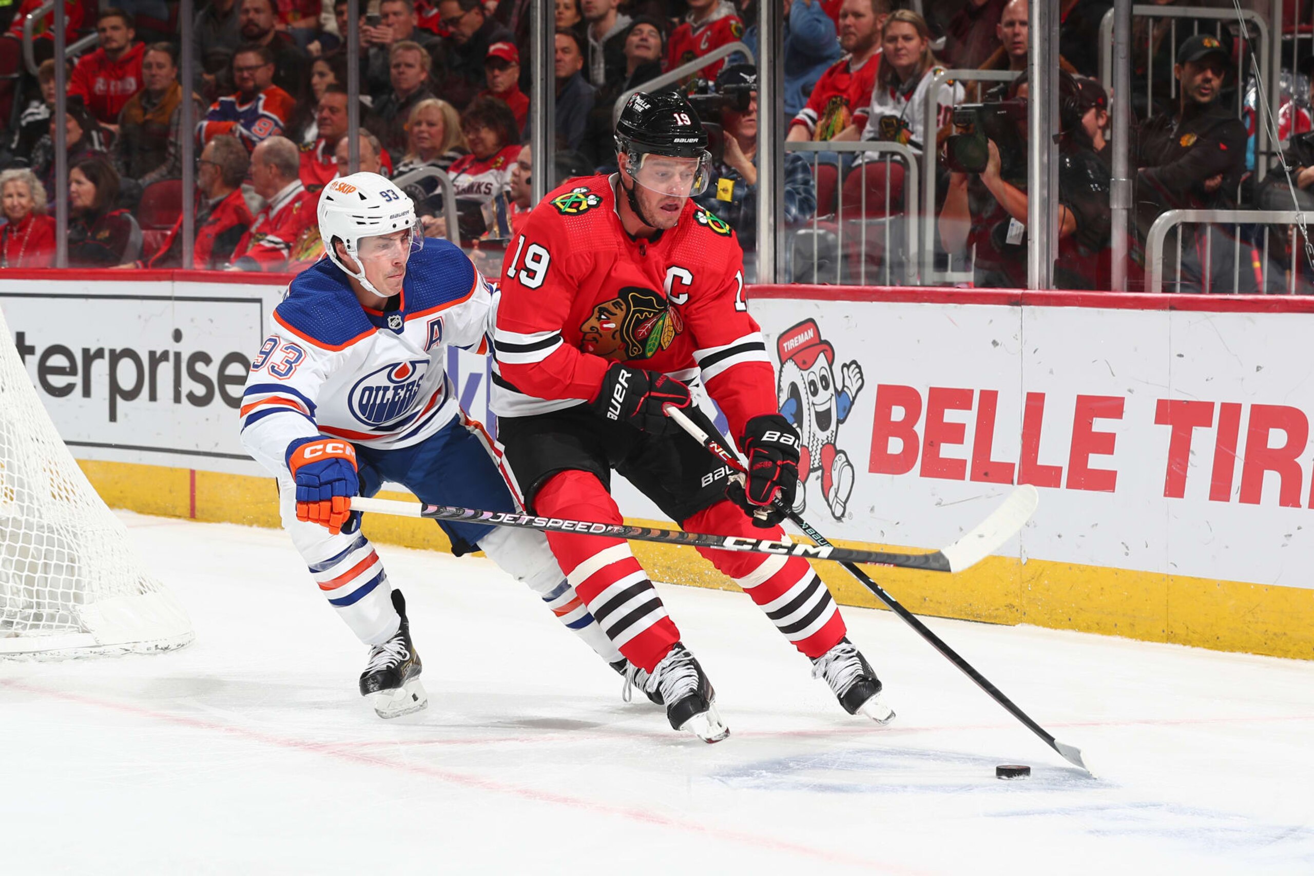 CHICAGO, ILLINOIS - NOVEMBER 30: Jonathan Toews #19 of the Chicago Blackhawks reaches for the puck ahead of Ryan Nugent-Hopkins #93 of the Edmonton Oilers in the first period at United Center on November 30, 2022 in Chicago, Illinois. (Photo by Chase Agnello-Dean/NHLI via Getty Images)