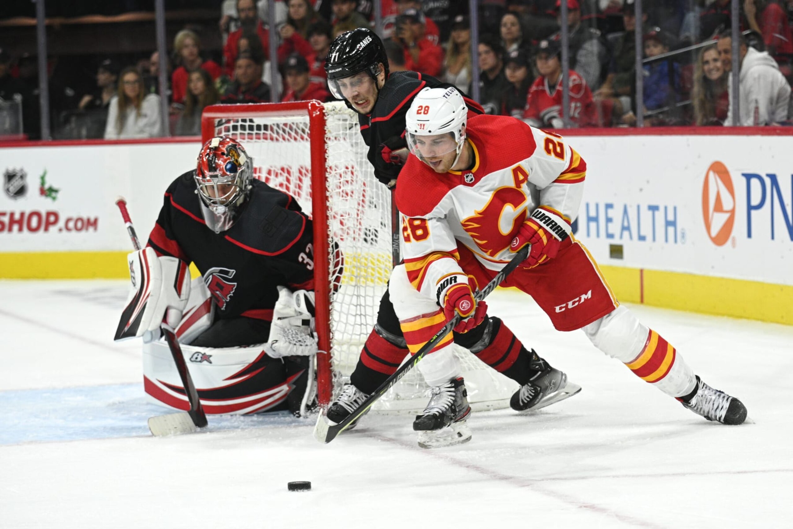 RALEIGH, NC - NOVEMBER 26: Calgary Flames Center Elias Lindholm (28) brings the puck around Carolina Hurricanes Right Wing Jesper Fast (71) and Goalie Antti Raanta (32) during the game between the Calgary Flames and the Carolina Hurricanes on November 26, 2022 at PNC Arena in Raleigh, North Carolina. (Photo by Katherine Gawlik/Icon Sportswire via Getty Images)