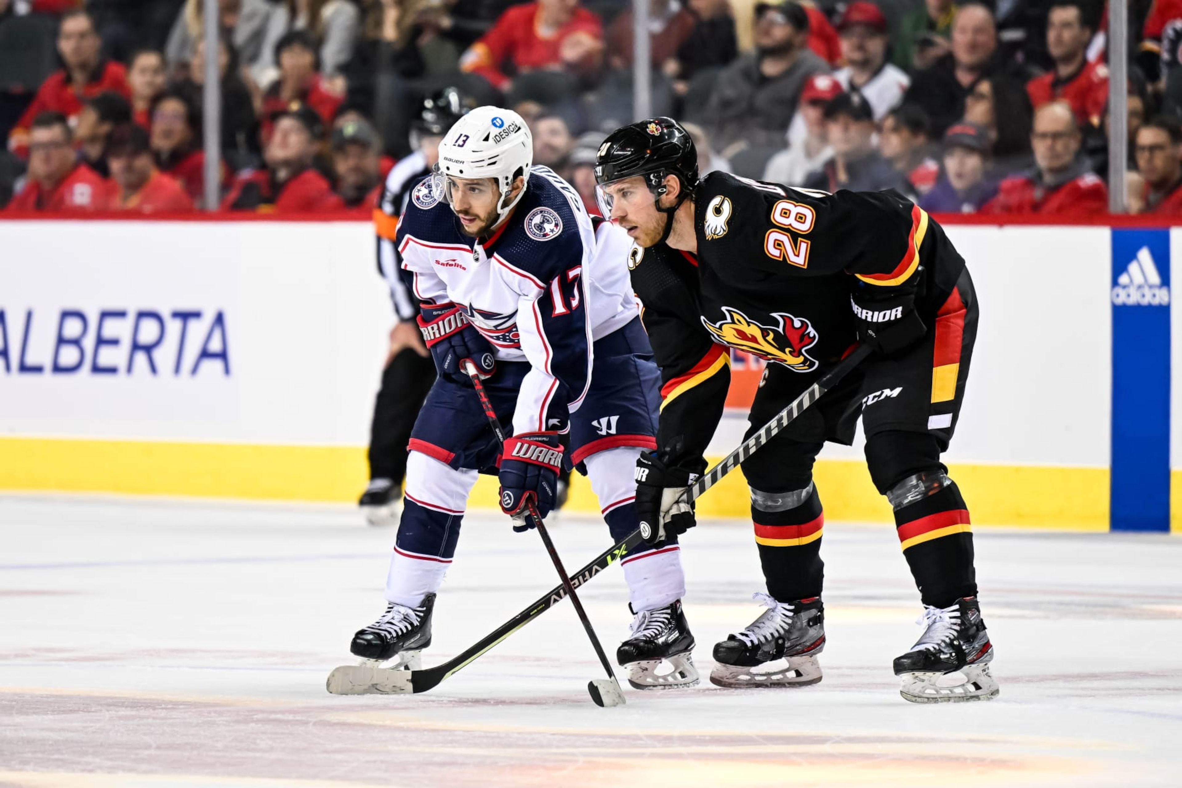CALGARY, AB - JANUARY 23: Columbus Blue Jackets Left Wing Johnny Gaudreau (13) and Calgary Flames Center Elias Lindholm (28) get set for a face-off during the overtime period of an NHL game between the Calgary Flames and the Columbus Blue Jackets on January 23, 2023, at the Scotiabank Saddledome in Calgary, AB. (Photo by Brett Holmes/Icon Sportswire via Getty Images)