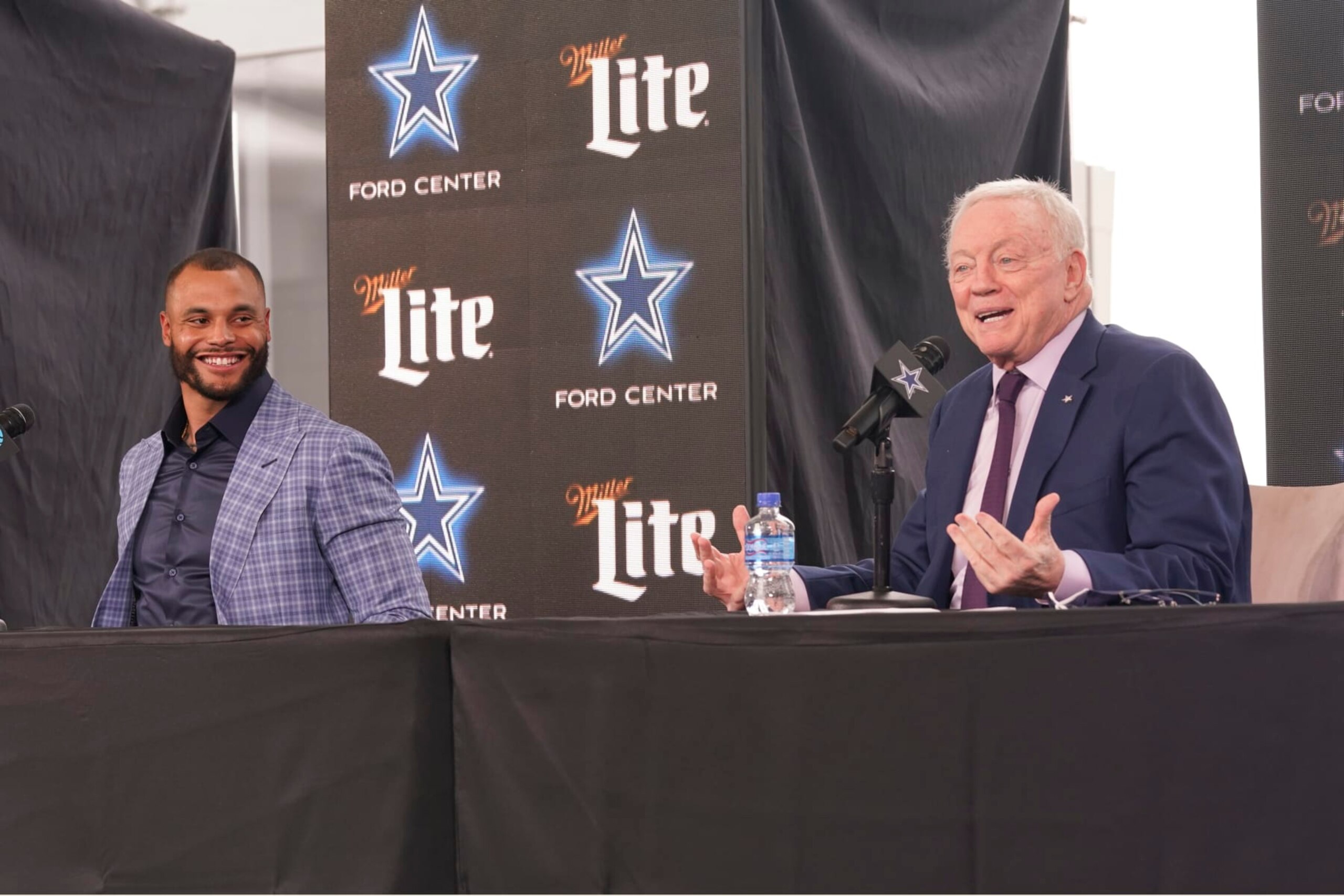 Dallas Cowboys quarterback Dak Prescott, left, looks on and smiles as team owner Jerry Jones speaks during a news conference at the team's NFL football practice facility in Frisco, Texas, Wednesday, March 10, 2021. The Cowboys and Prescott have finally agreed on the richest contract in club history, two years after negotiations began with the star quarterback. (AP Photo/LM Otero)