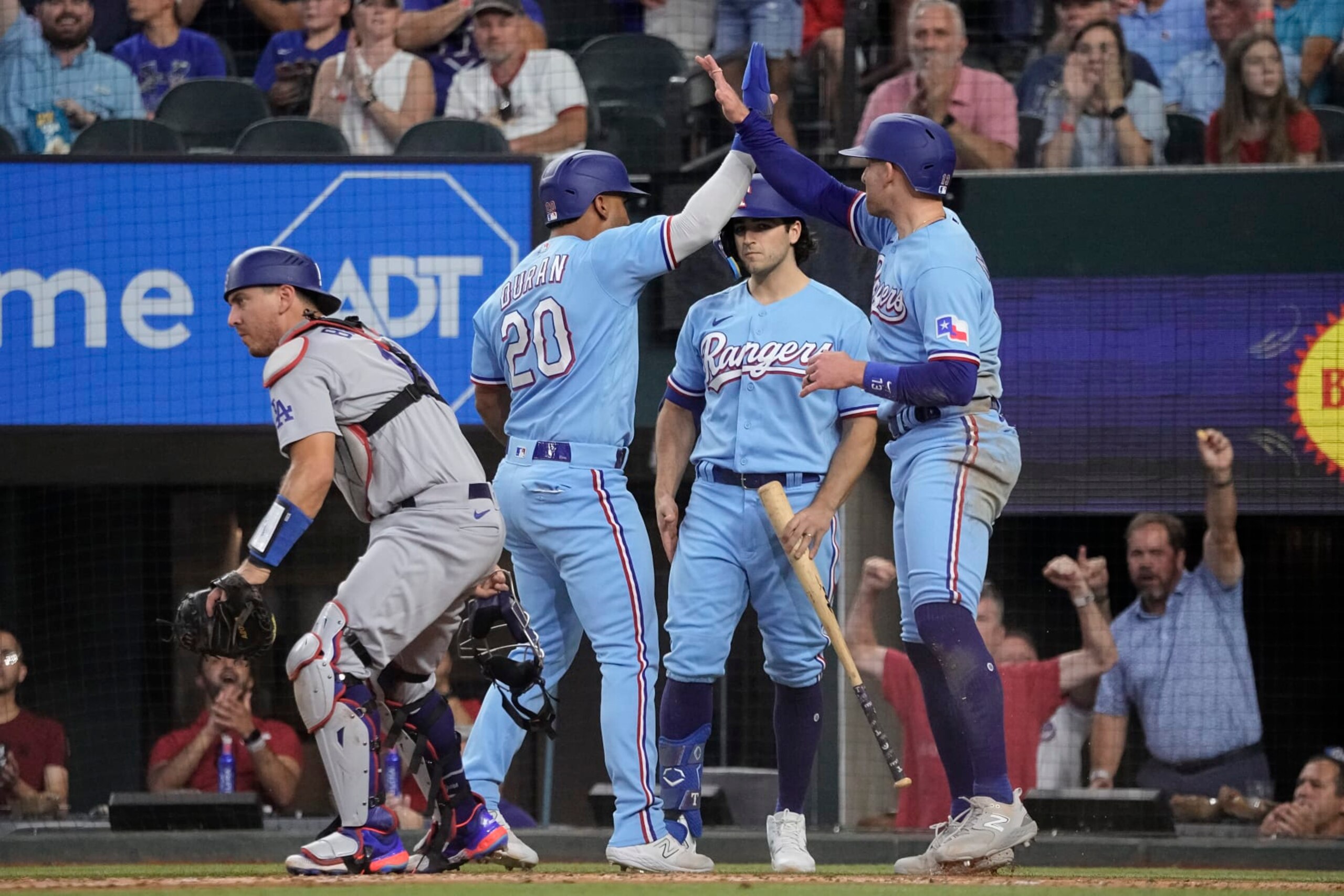 Ezequiel Duran (20) y Brad Miller, derecha, de los Rangers de Texas, celebran después de anotar con doble de Leody Taveras durante la tercera entrada del juego de béisbol en contra de los Dodgers de Los Ángeles, el domingo 23 de julio de 2023, en Arlington, Texas. (AP Foto/Sam Hodde)