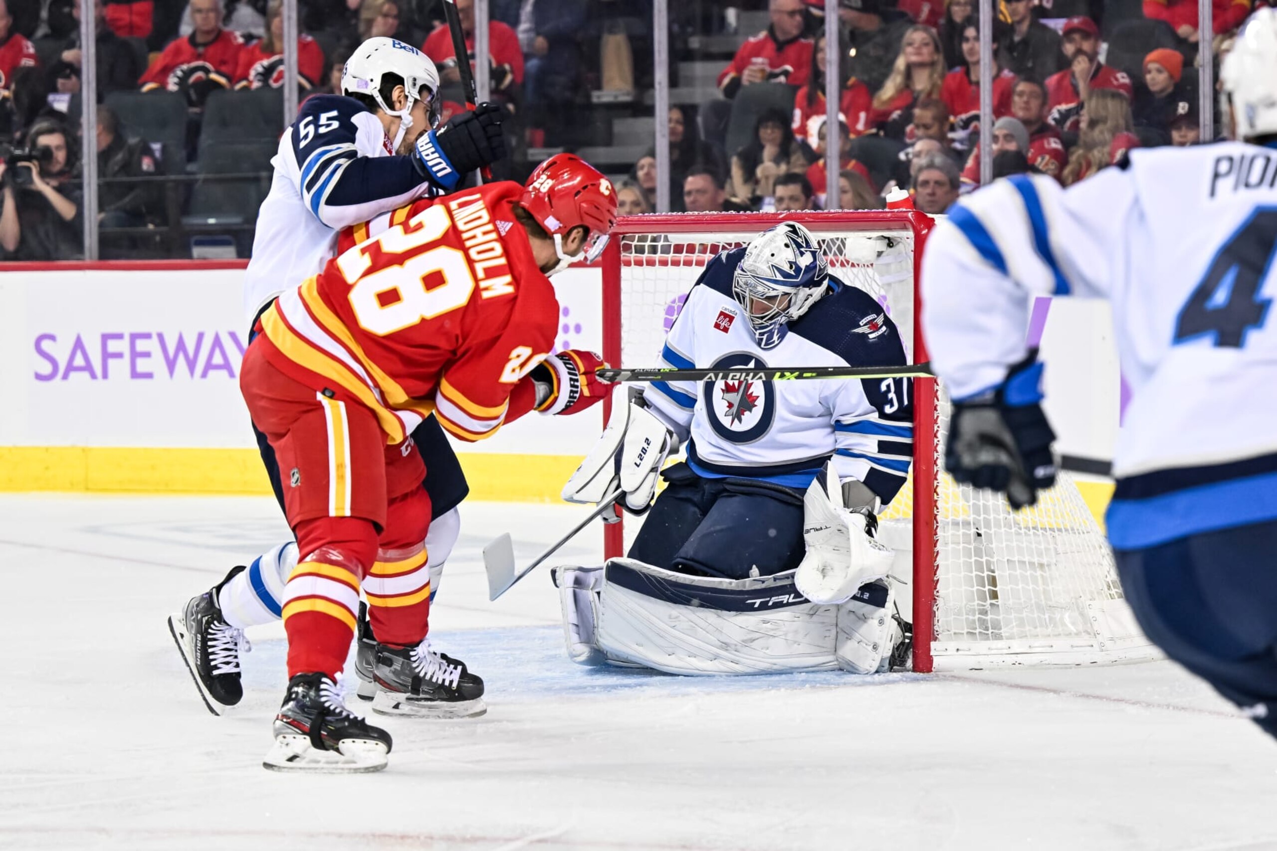 Calgary Flames center Elias Lindholm scores a goal against Winnipeg Jets goaltender Connor Hellebuyck. 