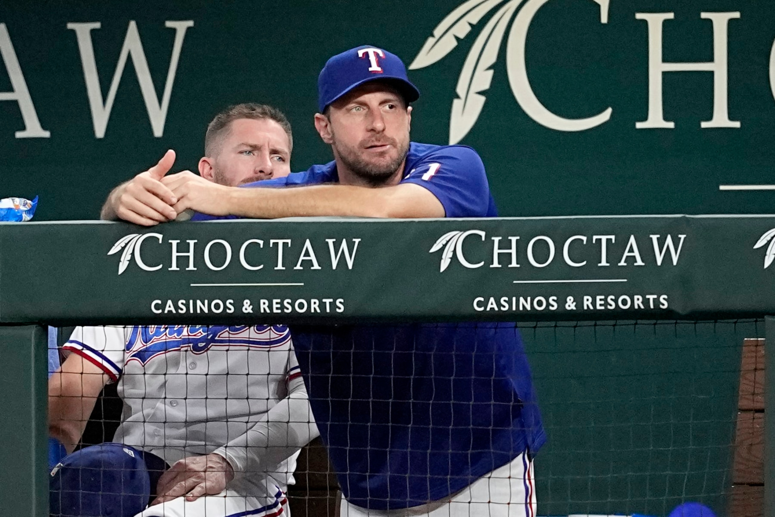 Texas Rangers newly acquired pitcher Max Scherzer, center, watches play from the dugout in the second inning of a baseball game against the Chicago White Sox, Tuesday, Aug. 1, 2023, in Arlington, Texas. (AP Photo/Tony Gutierrez)