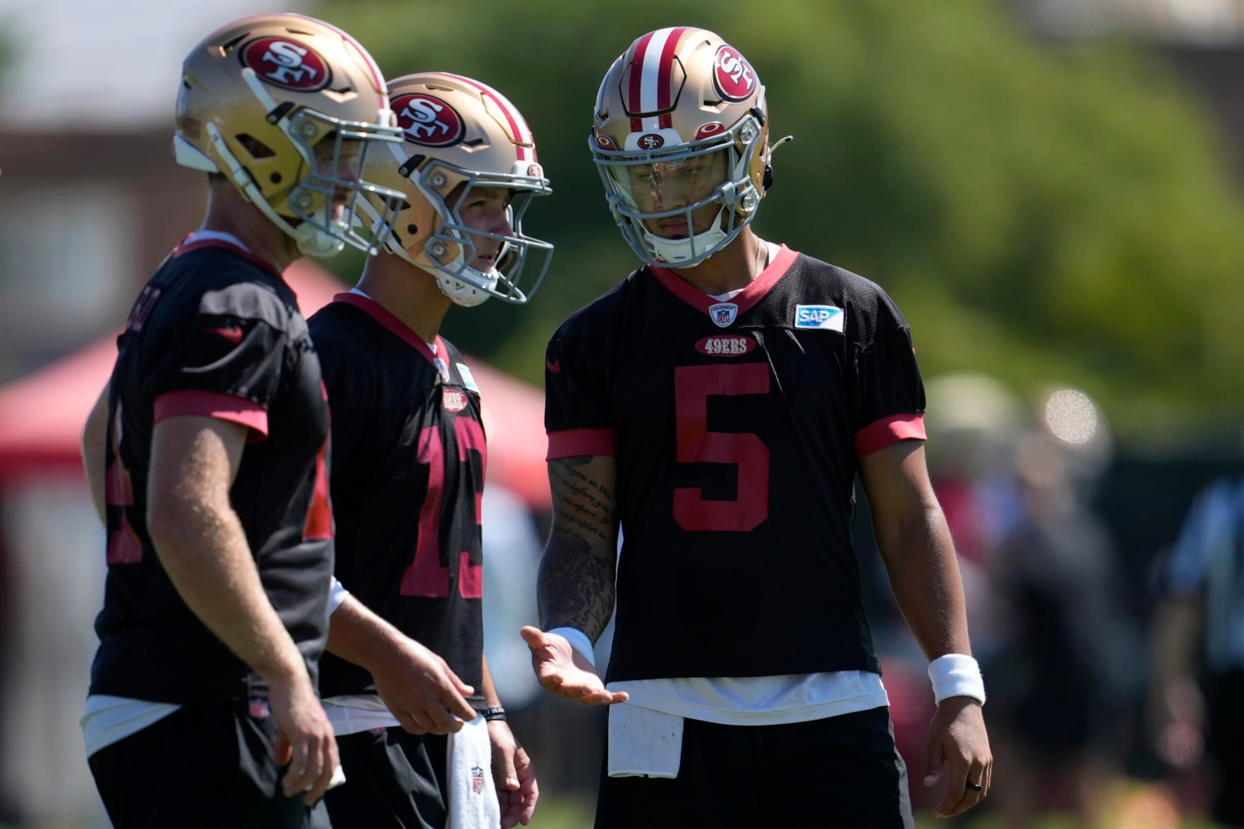 San Francisco 49ers quarterbacks Sam Darnold, left, Brock Purdy, middle, and Trey Lance (5) stand on the field during the NFL team's football training camp in Santa Clara, Calif., Thursday, July 27, 2023. (AP Photo/Jeff Chiu)