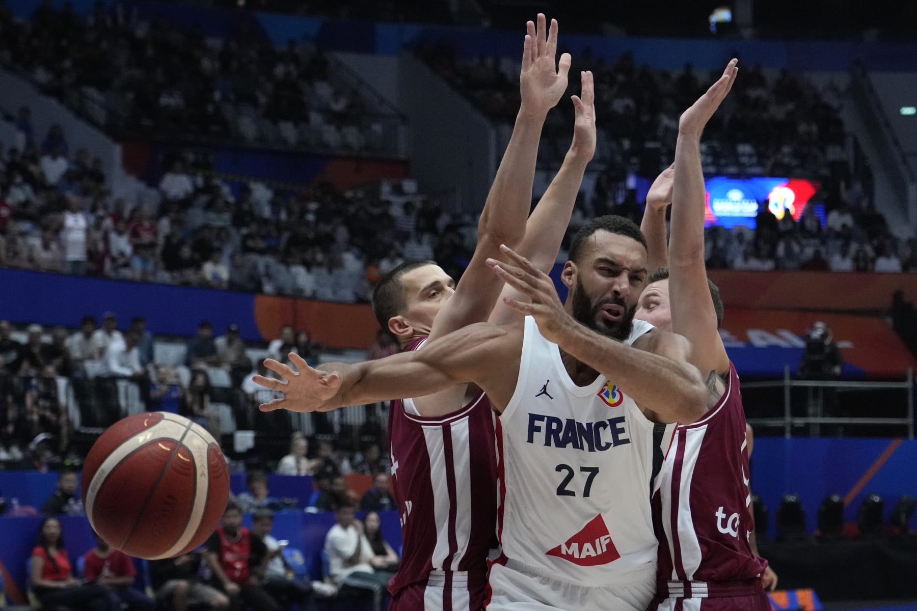 France center Rudy Gobert (27) drives against Latvia forward Andrejs Grazulis (24), left, and guard Dairis Bertans (9) during the Basketball World Cup group H match between France and Latvia at the Indonesia Arena stadium in Jakarta, Indonesia Sunday, Aug. 27, 2023. (AP Photo/Achmad Ibrahim)