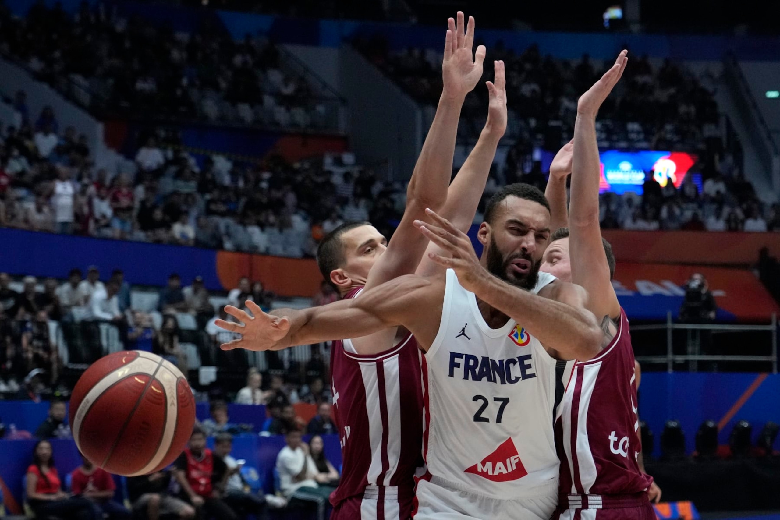 France center Rudy Gobert (27) drives against Latvia forward Andrejs Grazulis (24), left, and guard Dairis Bertans (9) during the Basketball World Cup group H match between France and Latvia at the Indonesia Arena stadium in Jakarta, Indonesia Sunday, Aug. 27, 2023. (AP Photo/Achmad Ibrahim)