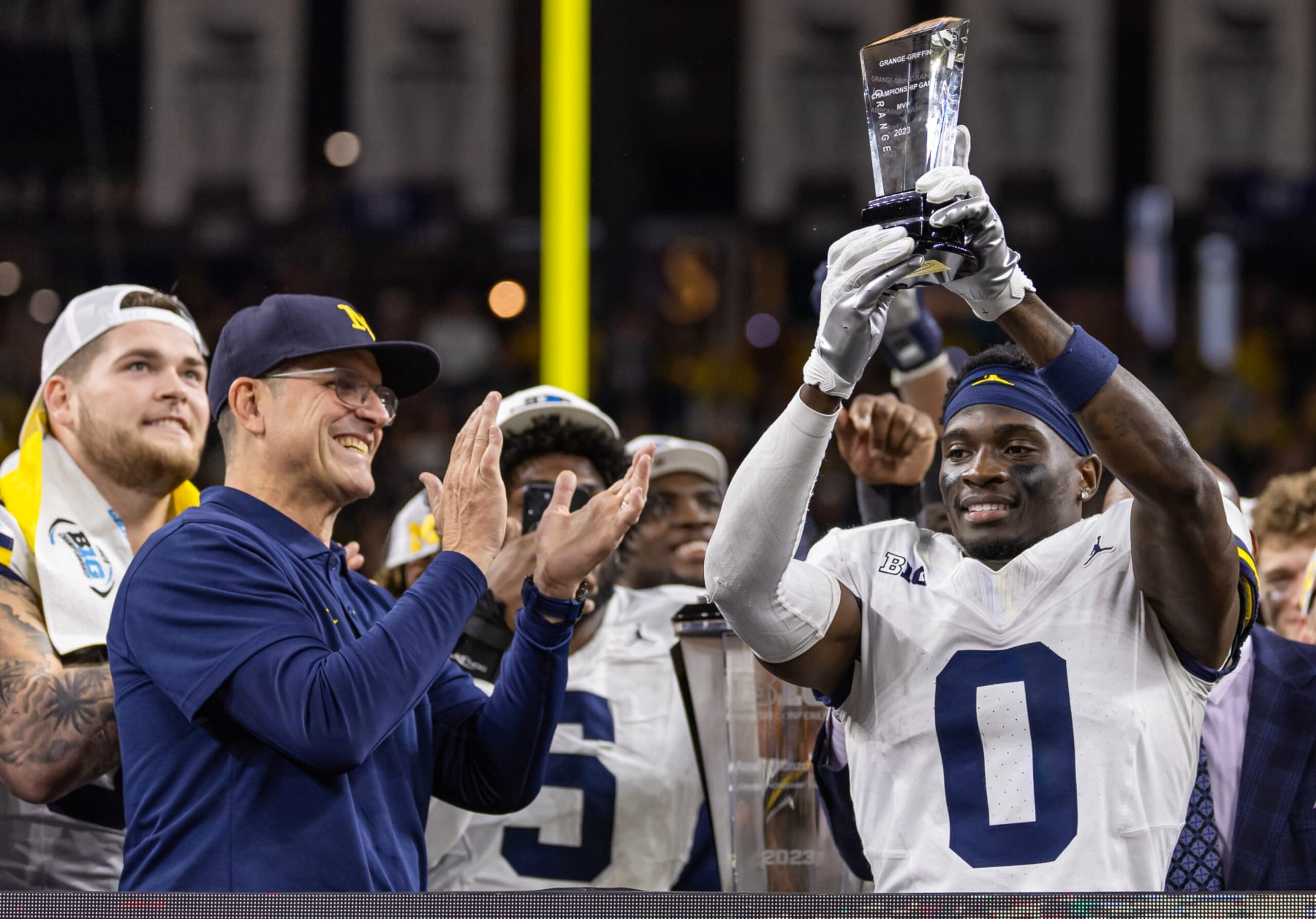 INDIANAPOLIS, INDIANA - DECEMBER 2: Head coach Jim Harbaugh applauds as Mike Sainristil #0 of the Michigan Wolverines holds up the MVP trophy following the Big Ten Championship against the Iowa Hawkeyes at Lucas Oil Stadium on December 2, 2023 in Indianapolis, Indiana. (Photo by Michael Hickey/Getty Images)