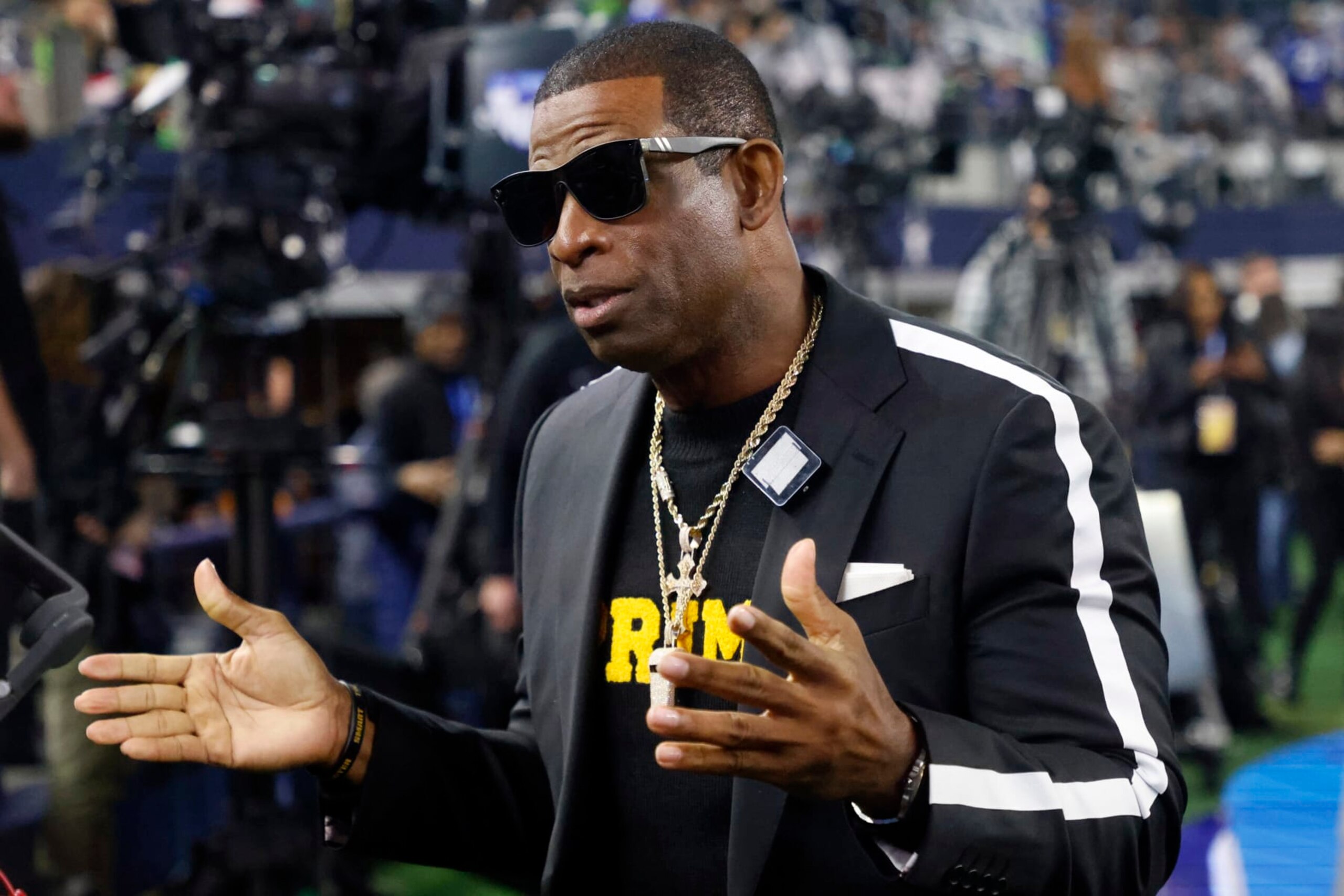 Colorado head football coach Deion Sanders talks with persons on the sideline before an NFL football game between the Seattle Seahawks and Dallas Cowboys in Arlington, Texas, Thursday, Nov. 30, 2023. (AP Photo/Michael Ainsworth)