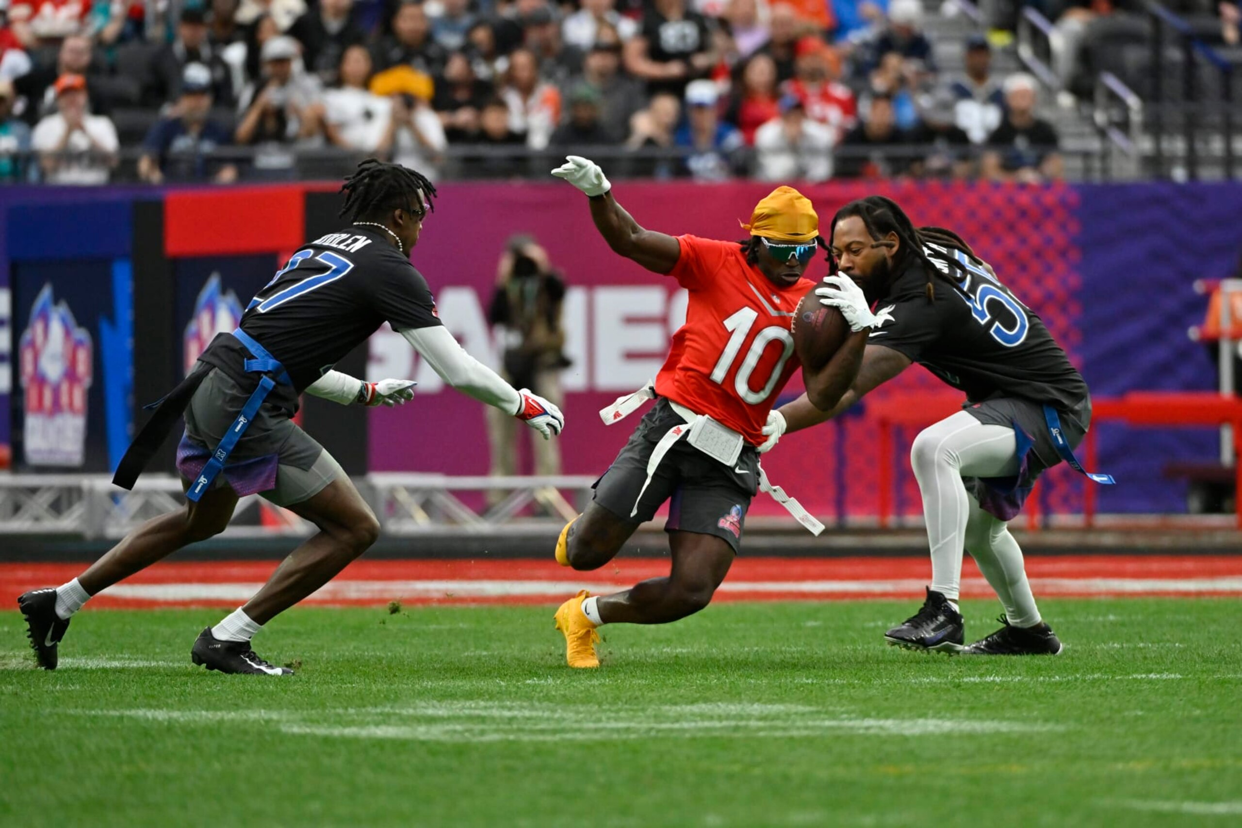 FILE - AFC wide receiver Tyreek Hill (10) of the Miami Dolphins carries the ball against NFC cornerback Tariq Woolen (27) of the Seattle Seahawks and outside linebacker Za'Darius Smith (55) of the Minnesota Vikings during the flag football event at the NFL Pro Bowl, Sunday, Feb. 5, 2023, in Las Vegas. The folks who allowed 3-on-3 basketball — also known as pick-up games at the local Y — into their grandiose spectacle and went along with the idea of handing out gold medals next summer for breakdancing are trying to lock down which new sports make the cut for the 2028 Los Angeles Games. Nine are under consideration, but the one that caught my eye was the flagged, non-contact version of the game that dominates the American sporting landscape but is barely a blip to the rest of the world. (AP Photo/David Becker, File)