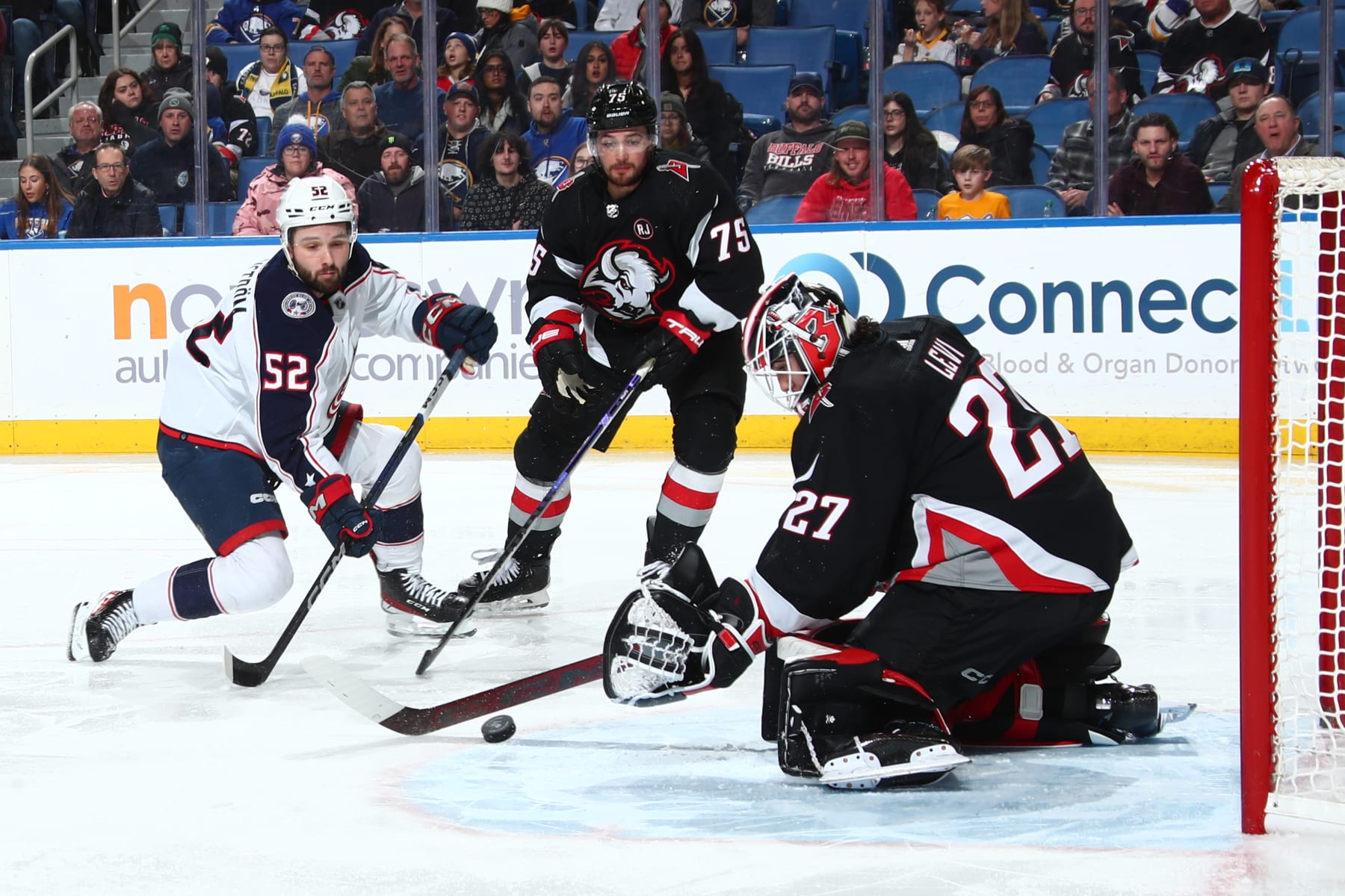 BUFFALO, NEW YORK - DECEMBER 19: Emil Bemstrom #52 of the Columbus Blue Jackets is defended by Devon Levi #27 and Connor Clifton #75 of the Buffalo Sabres during an NHL game on December 19, 2023 at KeyBank Center in Buffalo, New York. (Photo by Bill Wippert/NHLI via Getty Images)