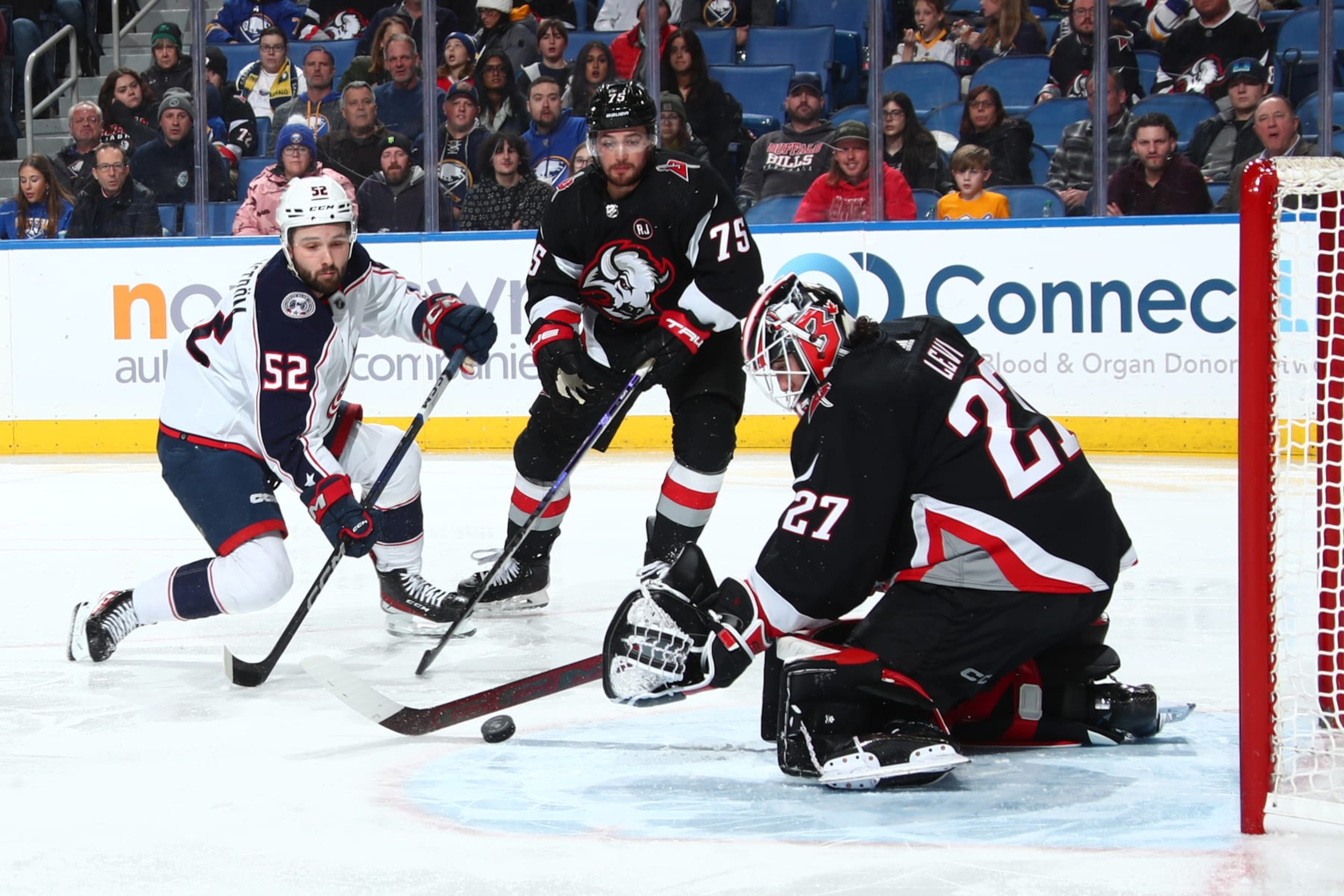 BUFFALO, NEW YORK - DECEMBER 19: Emil Bemstrom #52 of the Columbus Blue Jackets is defended by Devon Levi #27 and Connor Clifton #75 of the Buffalo Sabres during an NHL game on December 19, 2023 at KeyBank Center in Buffalo, New York. (Photo by Bill Wippert/NHLI via Getty Images) BUFFALO, NEW YORK - DECEMBER 19: Emil Bemstrom #52 of the Columbus Blue Jackets is defended by Devon Levi #27 and Connor Clifton #75 of the Buffalo Sabres during an NHL game on December 19, 2023 at KeyBank Center in Buffalo, New York. (Photo by Bill Wippert/NHLI via Getty Images)