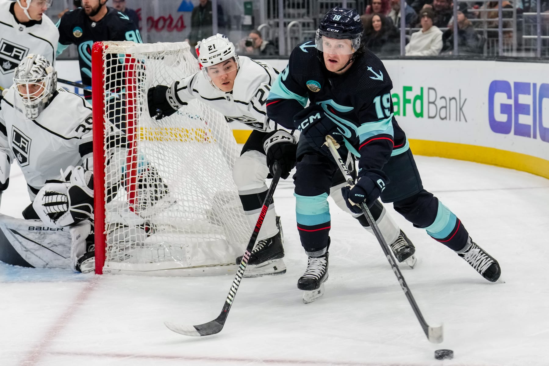SEATTLE, WASHINGTON - DECEMBER 16: Jordan Spence #21 of the Los Angeles Kings challenges Jared McCann #19 of the Seattle Kraken for the puck during the first period of a game at Climate Pledge Arena on December 16, 2023 in Seattle, Washington. (Photo by Christopher Mast/NHLI via Getty Images)