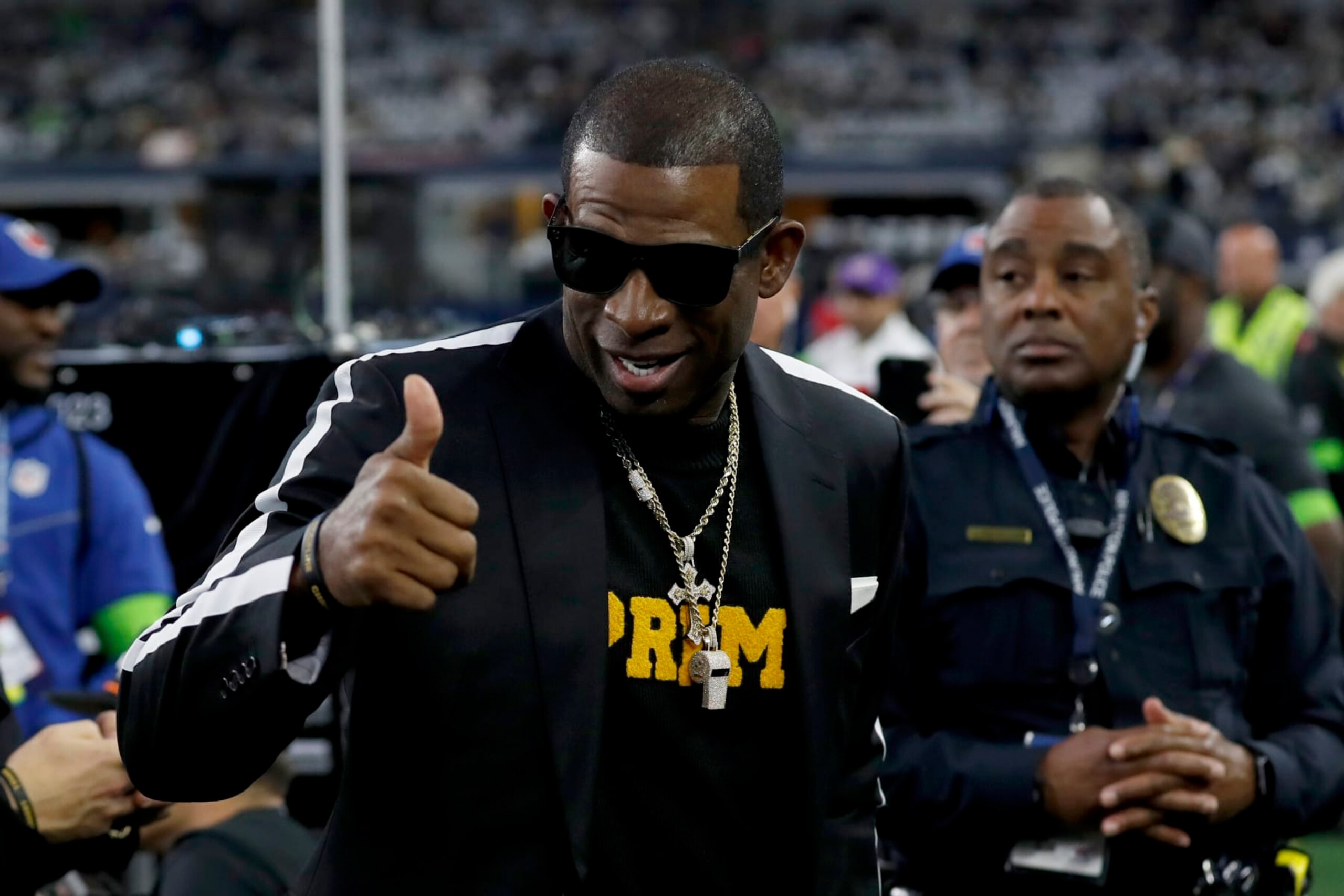 Colorado head football coach Deion Sanders, talks with persons on the sideline before the first half of an NFL football game between the Seattle Seahawks and Dallas Cowboys in Arlington, Texas, Thursday, Nov. 30, 2023. (AP Photo/Roger Steinman)