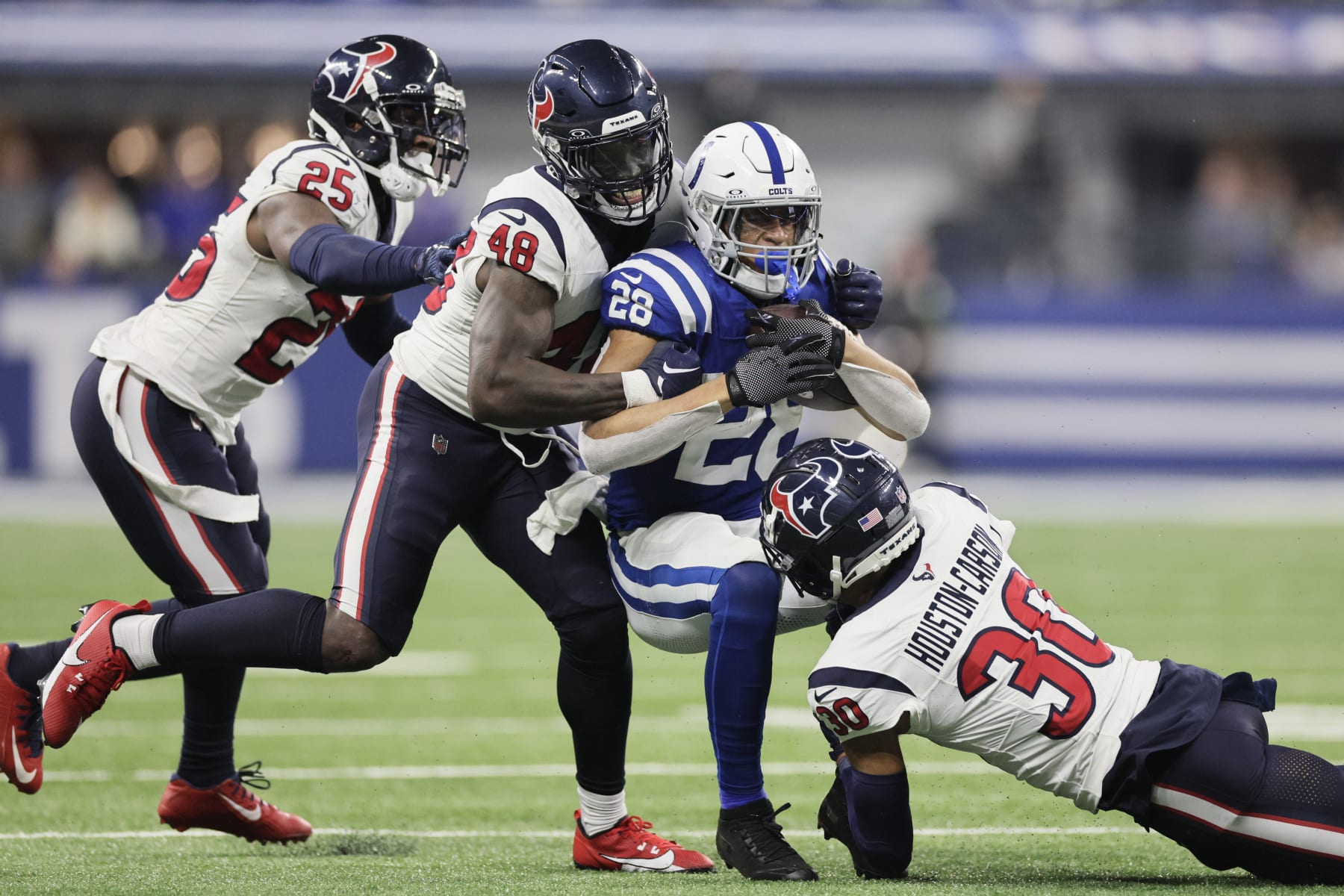 INDIANAPOLIS, INDIANA - JANUARY 06: Jonathan Taylor #28 of the Indianapolis Colts is tackled by DeAndre Houston-Carson #30 and Christian Harris #48 of the Houston Texans during the first quarter at Lucas Oil Stadium on January 06, 2024 in Indianapolis, Indiana. (Photo by Andy Lyons/Getty Images)