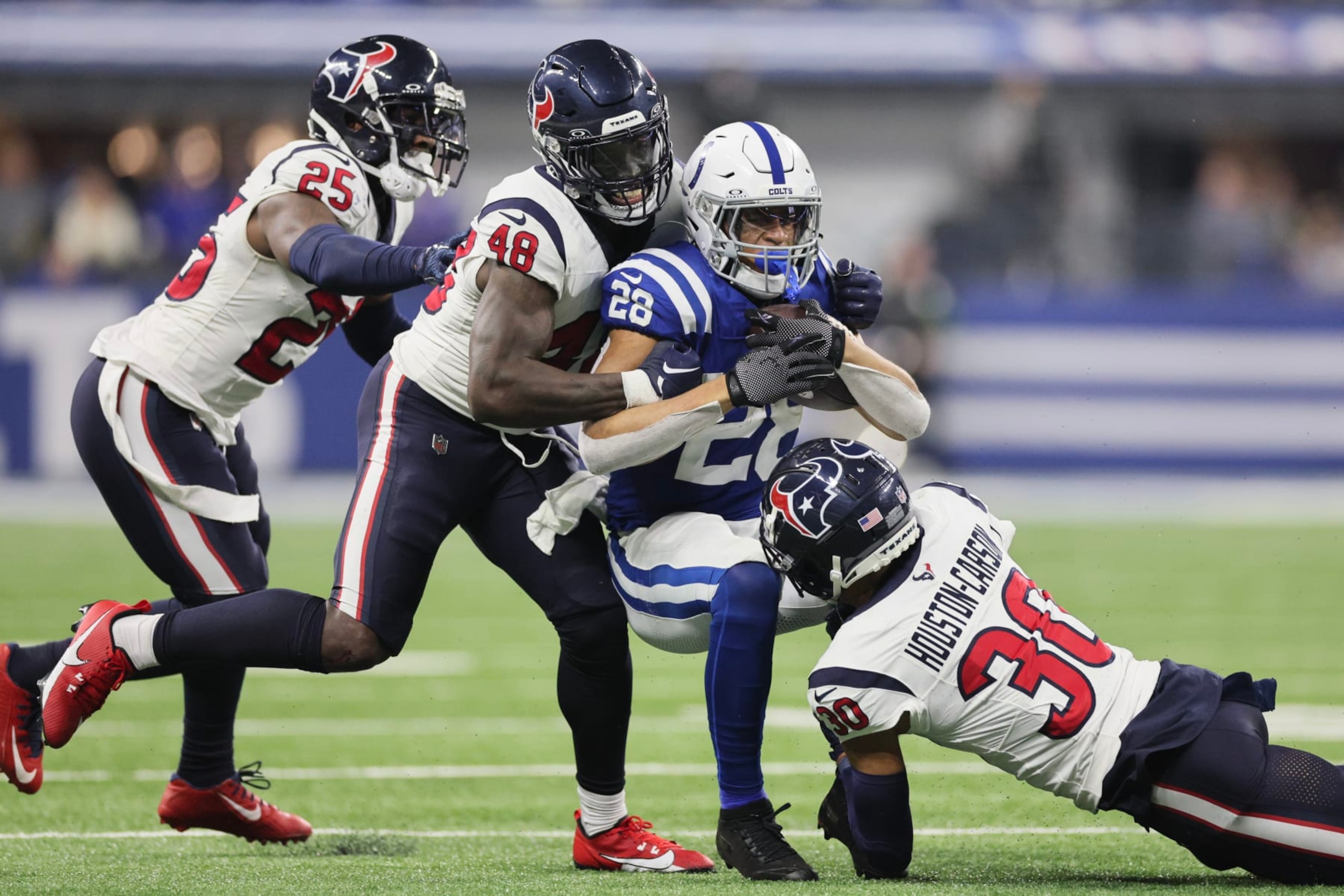 INDIANAPOLIS, INDIANA - JANUARY 06: Jonathan Taylor #28 of the Indianapolis Colts is tackled by DeAndre Houston-Carson #30 and Christian Harris #48 of the Houston Texans during the first quarter at Lucas Oil Stadium on January 06, 2024 in Indianapolis, Indiana. (Photo by Andy Lyons/Getty Images)