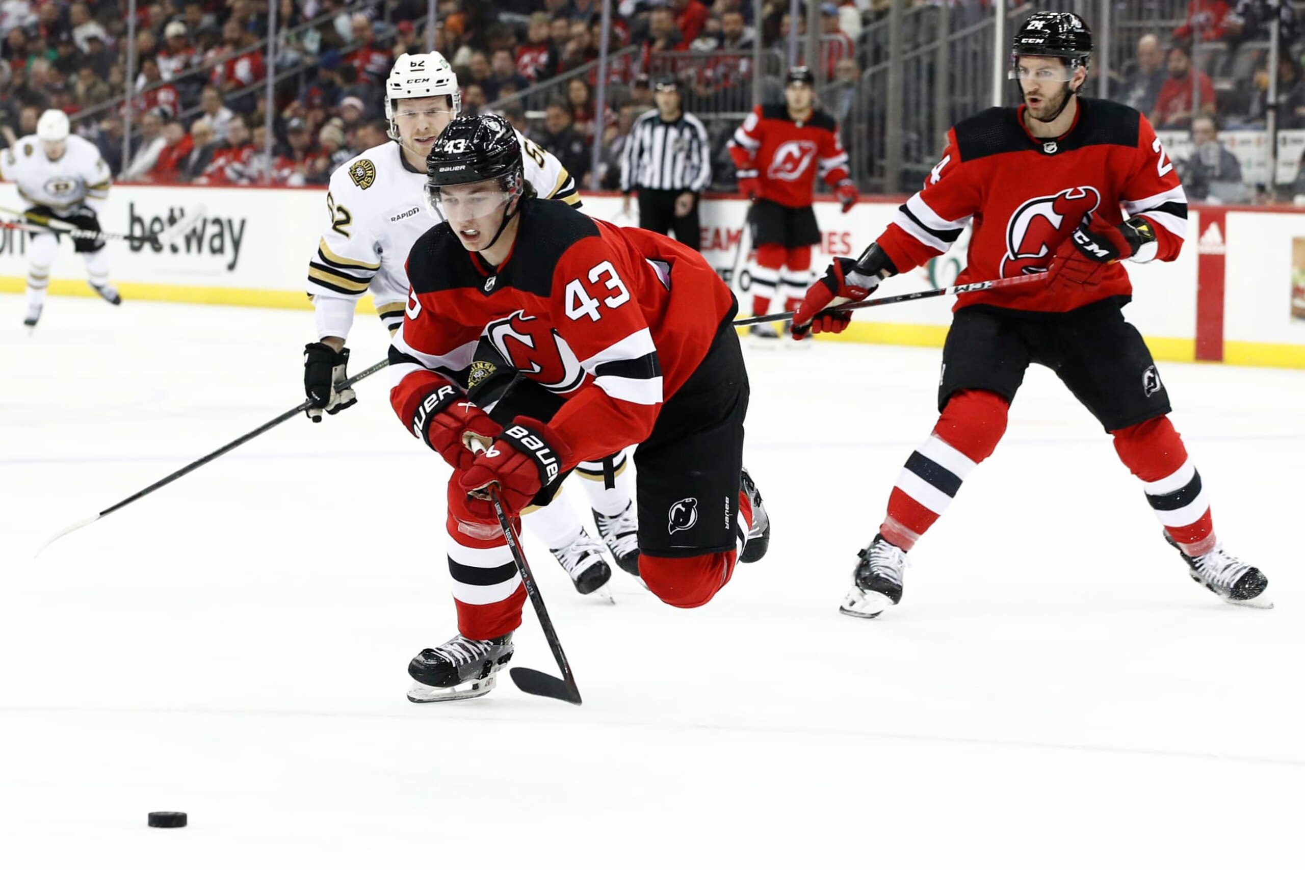 NEWARK, NEW JERSEY - DECEMBER 13: Luke Hughes #43 of the New Jersey Devils chases the puck as Oskar Steen #62 of the Boston Bruins defends during the first period at Prudential Center on December 13, 2023 in Newark, New Jersey. (Photo by Sarah Stier/Getty Images)