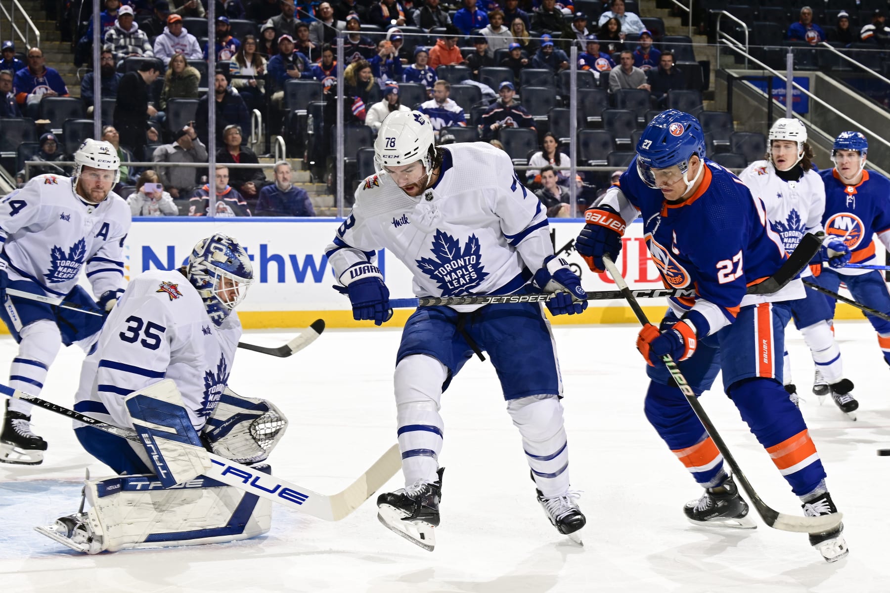 ELMONT, NEW YORK - DECEMBER 11:  TJ Brodie #78 of the Toronto Maple Leafs defends Anders Lee #27 of the New York Islanders as Ilya Samsonov #35 tends net during the first period at UBS Arena on December 11, 2023 in Elmont, New York. (Photo by Steven Ryan/NHLI via Getty Images)