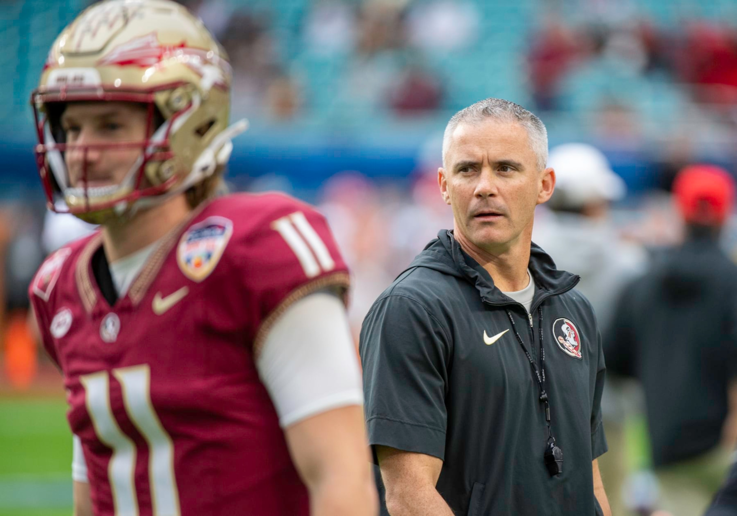 MIAMI GARDENS, FL - DECEMBER 30: Florida State head coach Mike Norvell walks behind Florida State quarterback Brock Glenn (11) as he warms up on the field before the Capital One Orange Bowl college football game between the Georgia Bulldogs and the Florida State Seminoles on December 30, 2023 at the Hard Rock Stadium in Miami Gardens, FL. (Photo by Doug Murray/Icon Sportswire via Getty Images)