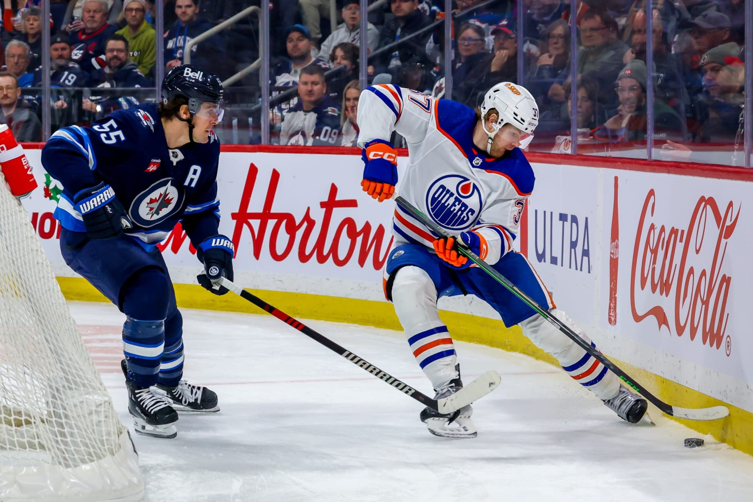 WINNIPEG, CANADA - NOVEMBER 30: Warren Foegele #37 of the Edmonton Oilers plays the puck away from Mark Scheifele #55 of the Winnipeg Jets during third period action at Canada Life Centre on November 30, 2023 in Winnipeg, Manitoba, Canada. (Photo by Jonathan Kozub/NHLI via Getty Images)