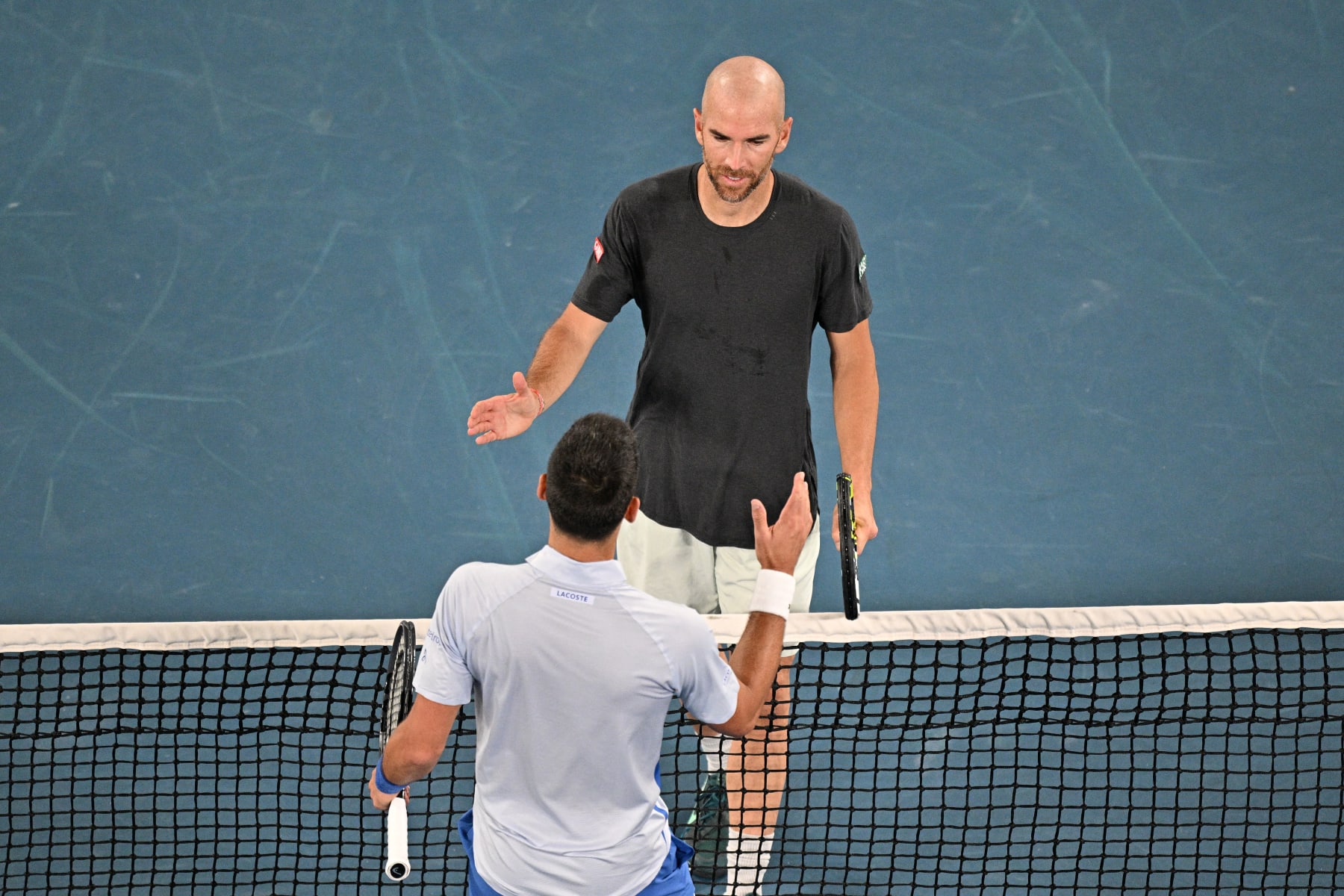 Serbia's Novak Djokovic (bottom) shakes hands with France's Adrian Mannarino after their men's singles match on day eight of the Australian Open tennis tournament in Melbourne on January 21, 2024. (Photo by Anthony WALLACE / AFP) / -- IMAGE RESTRICTED TO EDITORIAL USE - STRICTLY NO COMMERCIAL USE -- (Photo by ANTHONY WALLACE/AFP via Getty Images)