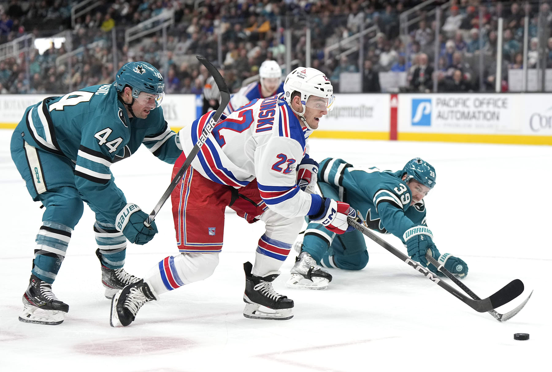 SAN JOSE, CALIFORNIA - JANUARY 23: Jonny Brodzinski #22 of the New York Rangers looks to attack the goal defended by Marc-Edouard Vlasic #44 and Logan Couture #39 of the San Jose Sharks during the first period at SAP Center on January 23, 2024 in San Jose, California. (Photo by Thearon W. Henderson/Getty Images)