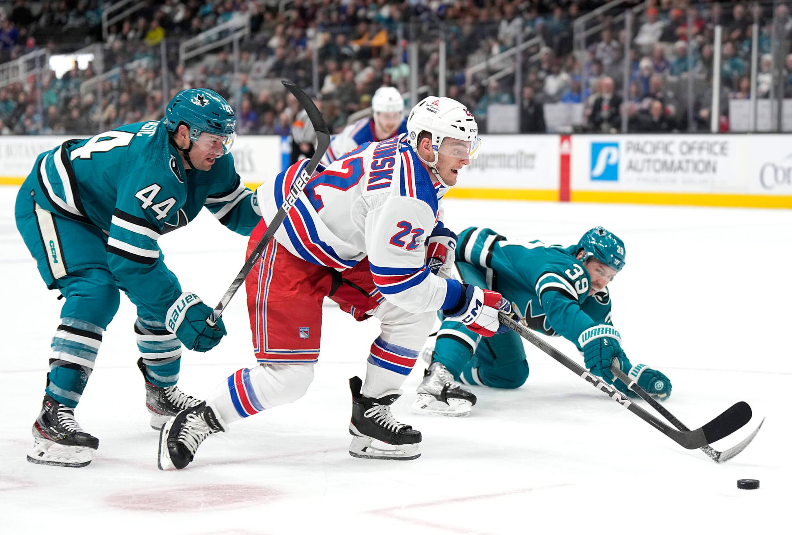 SAN JOSE, CALIFORNIA - JANUARY 23: Jonny Brodzinski #22 of the New York Rangers looks to attack the goal defended by Marc-Edouard Vlasic #44 and Logan Couture #39 of the San Jose Sharks during the first period at SAP Center on January 23, 2024 in San Jose, California. (Photo by Thearon W. Henderson/Getty Images)