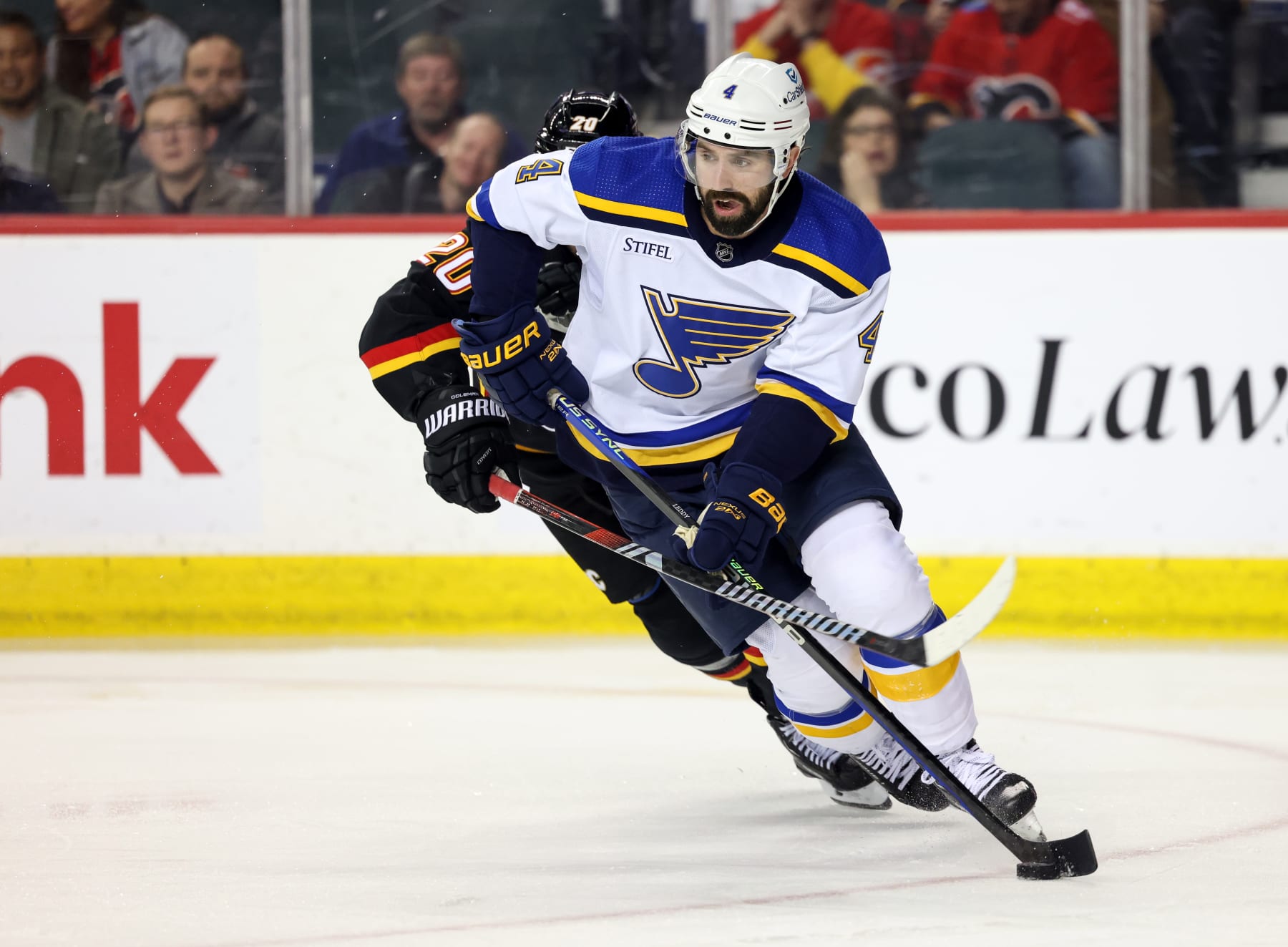 CALGARY, CANADA - JANUARY 23: Nick Leddy #4 of the St. Louis Blues skates the puck ahead of Blake Coleman #20 of the Calgary Flames battles for the puck during the third period at the Scotiabank Saddledome on January 23, 2024 in Calgary, Alberta, Canada. (Photo by Leah Hennel/Getty Images)