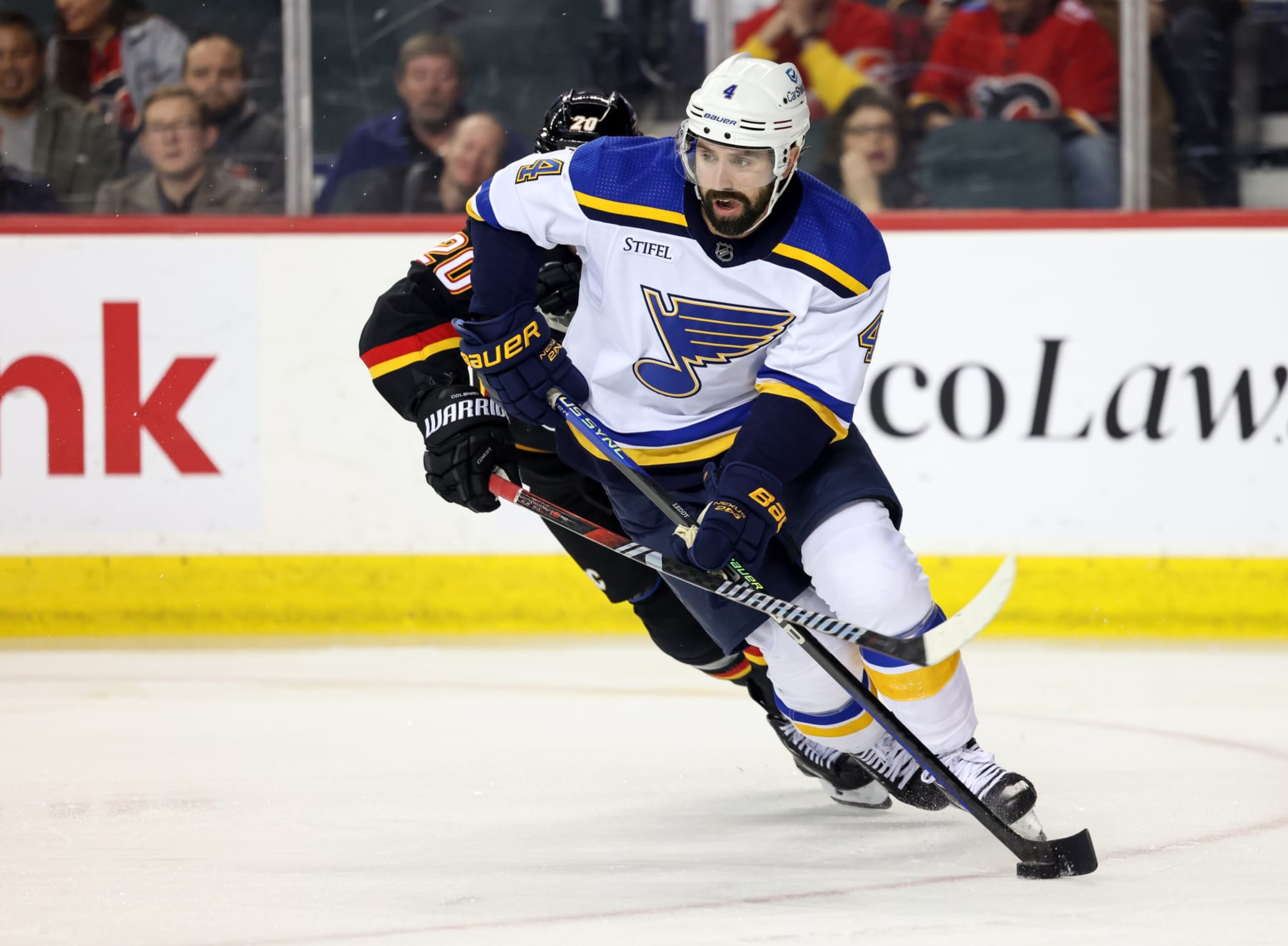 CALGARY, CANADA - JANUARY 23: Nick Leddy #4 of the St. Louis Blues skates the puck ahead of Blake Coleman #20 of the Calgary Flames battles for the puck during the third period at the Scotiabank Saddledome on January 23, 2024 in Calgary, Alberta, Canada. (Photo by Leah Hennel/Getty Images)
