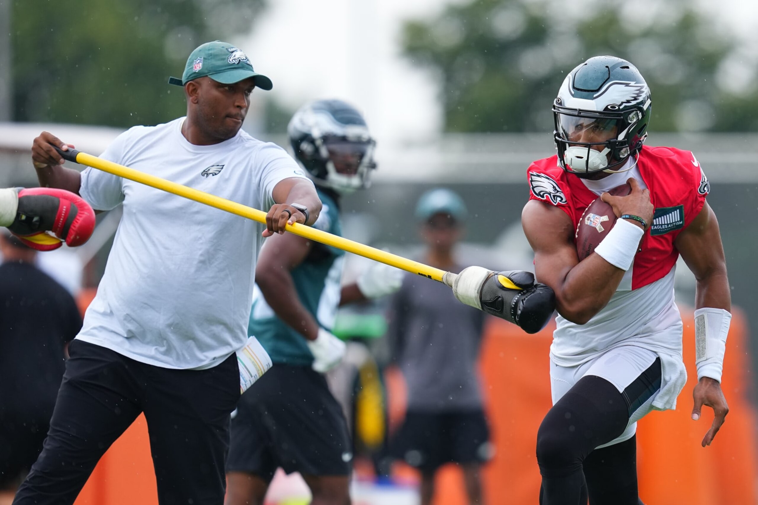 PHILADELPHIA, PENNSYLVANIA - AUGUST 10: Jalen Hurts #1 of the Philadelphia Eagles runs with the ball as offensive coordinator Brian Johnson tries to punch the ball out during Training Camp at the NovaCare Complex on August 10, 2023 in Philadelphia, Pennsylvania. (Photo by Mitchell Leff/Getty Images)